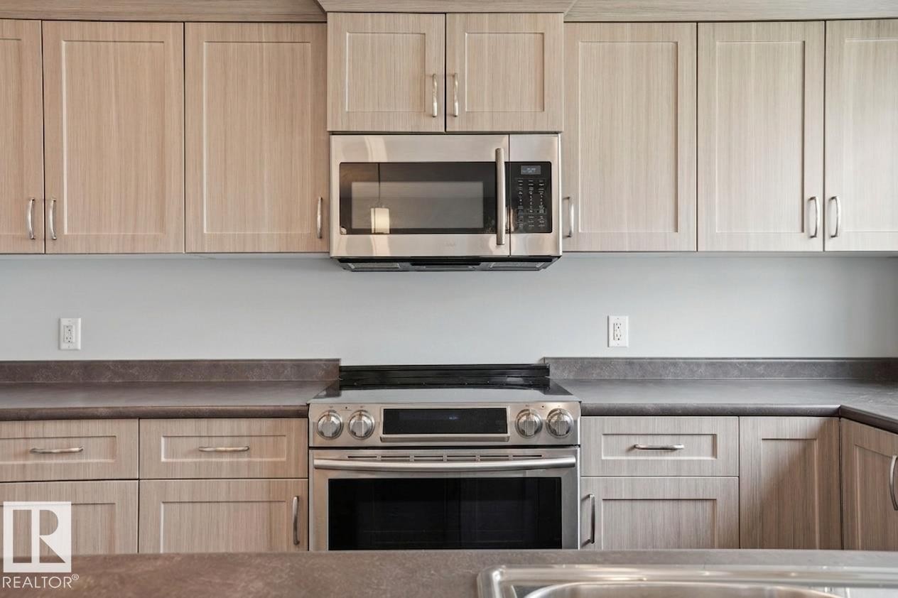 Light wood-finish cabinetry, stainless steel range, stainless steel microwave, and dark countertops - #12 1391 Starling Dr Nw, Edmonton, AB