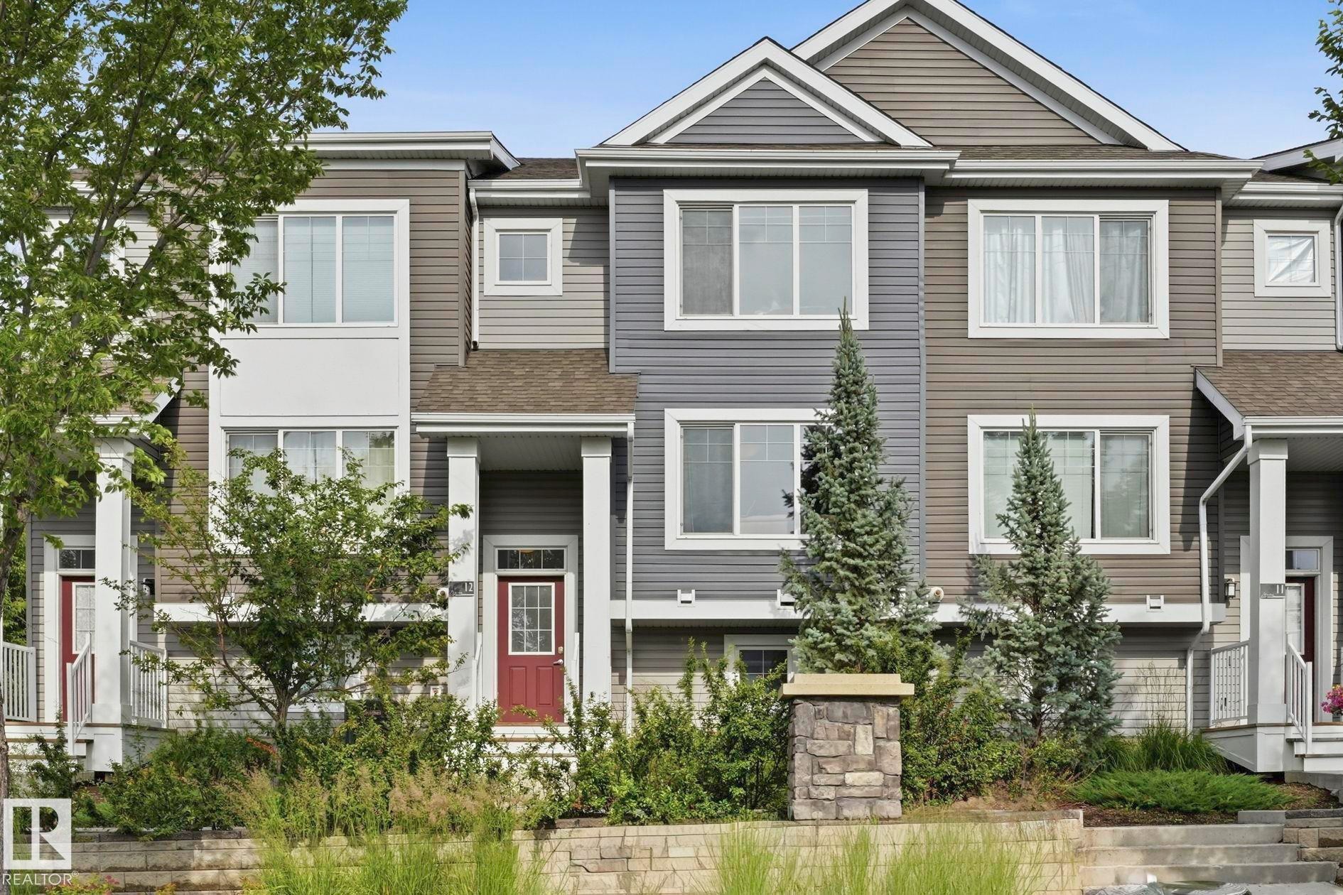 Multi-level townhouse exterior featuring multiple window styles, columns at the entry, and an integrated landscaping bed with plantings - #12 1391 Starling Dr Nw, Edmonton, AB