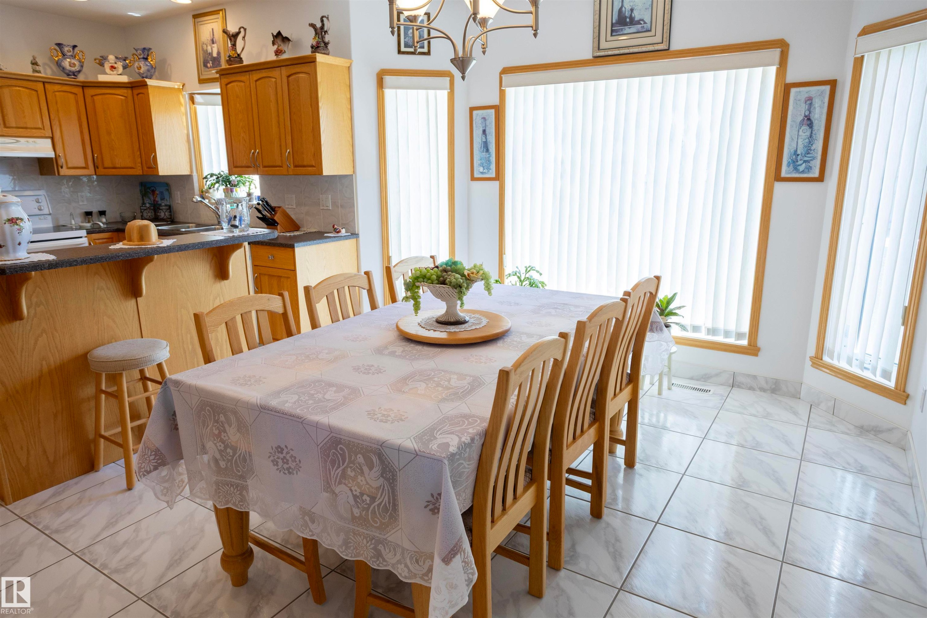 Well-lit kitchen and dining area featuring light wood cabinetry, a breakfast bar, and tiled flooring - 6407 163 Avenue Nw, Edmonton, AB