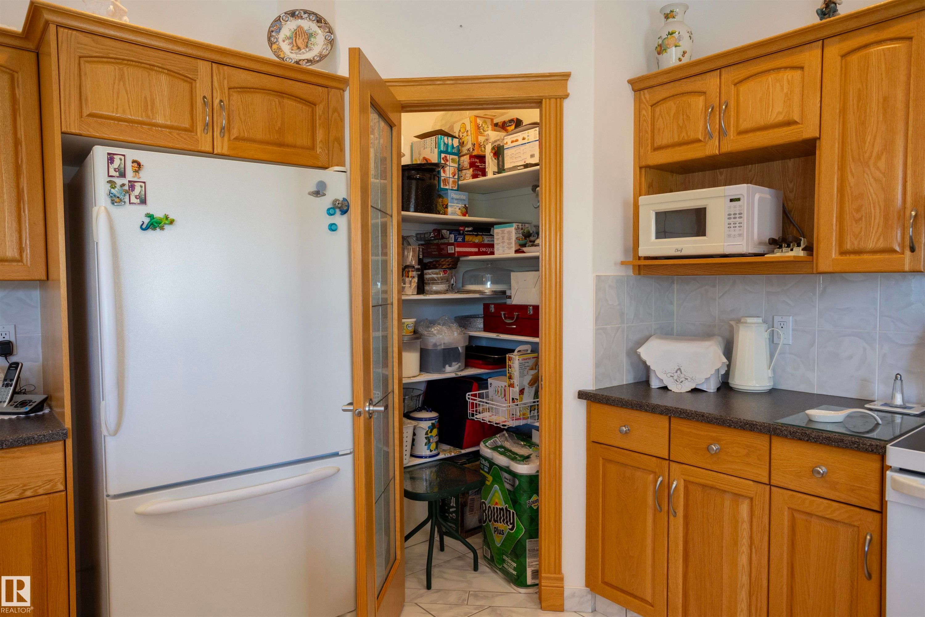 Kitchen featuring light wood-finish cabinetry, a freestanding refrigerator, and a pantry with a wood-frame glass door - 6407 163 Avenue Nw, Edmonton, AB