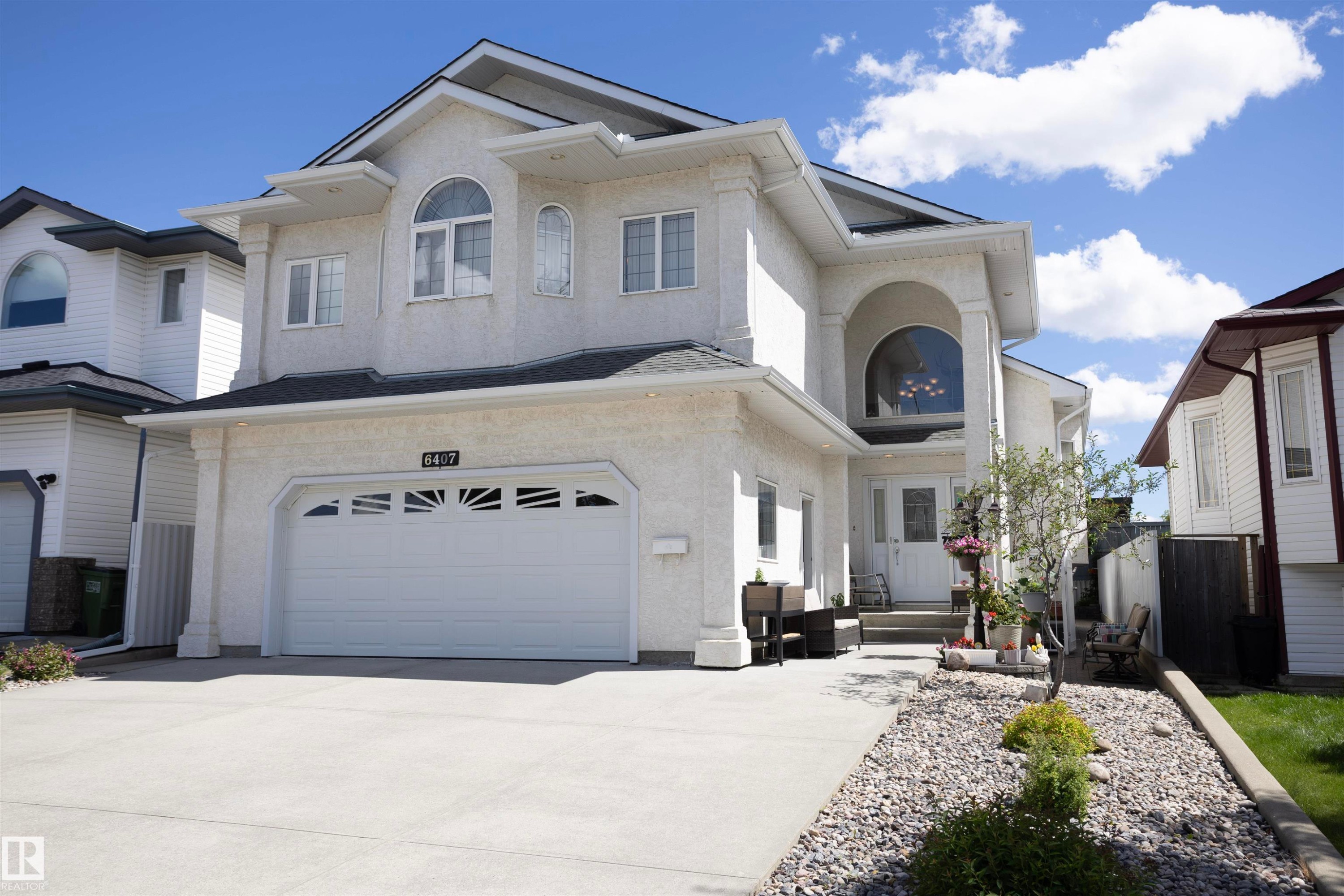 Two-story stucco exterior featuring an arched entryway with decorative transom window, an attached two-car garage with sunburst window detailing, and a concrete driveway - 6407 163 Avenue Nw, Edmonton, AB