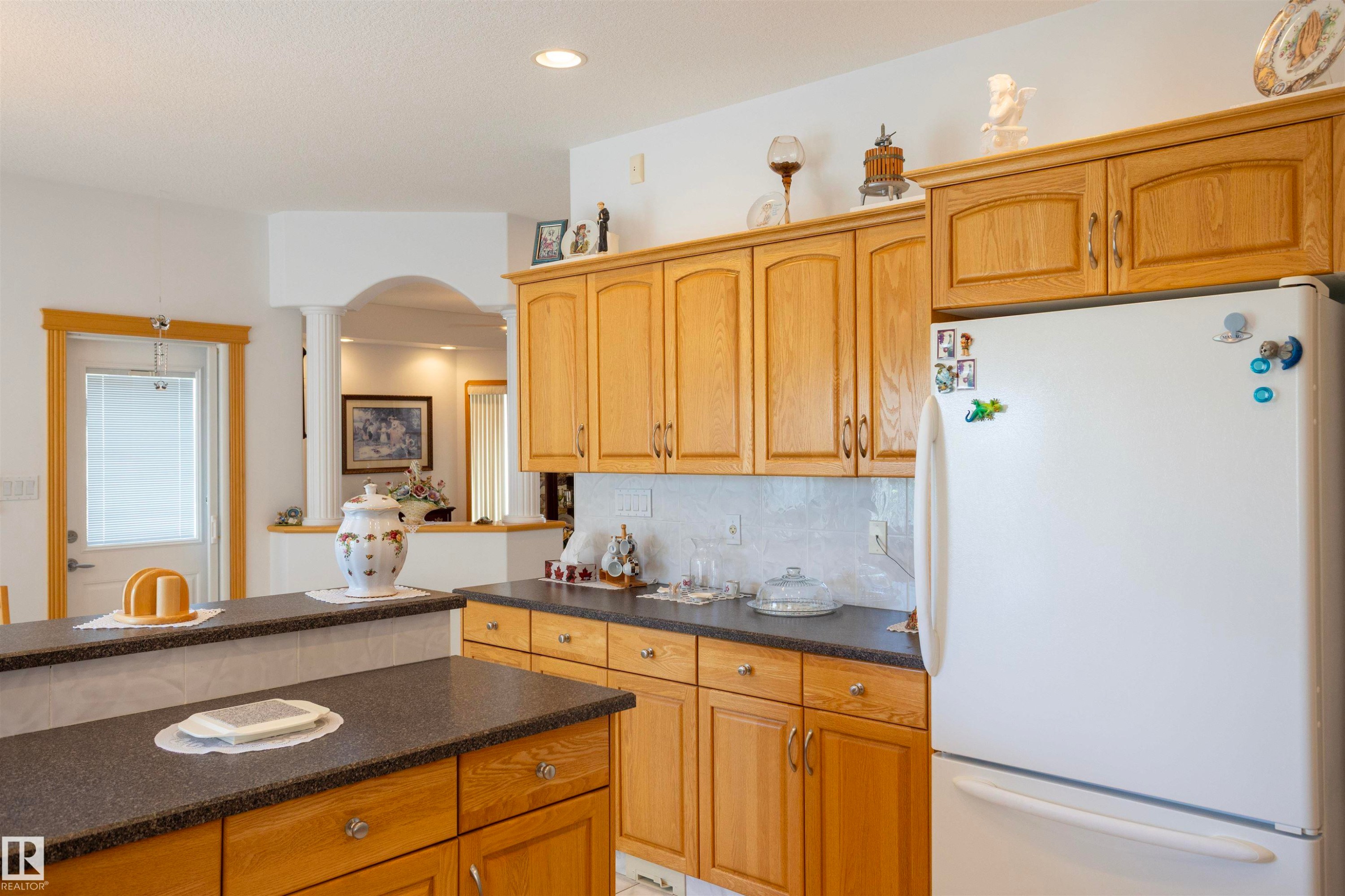 Kitchen with wood-finish cabinetry, dark countertops, and a white refrigerator - 6407 163 Avenue Nw, Edmonton, AB