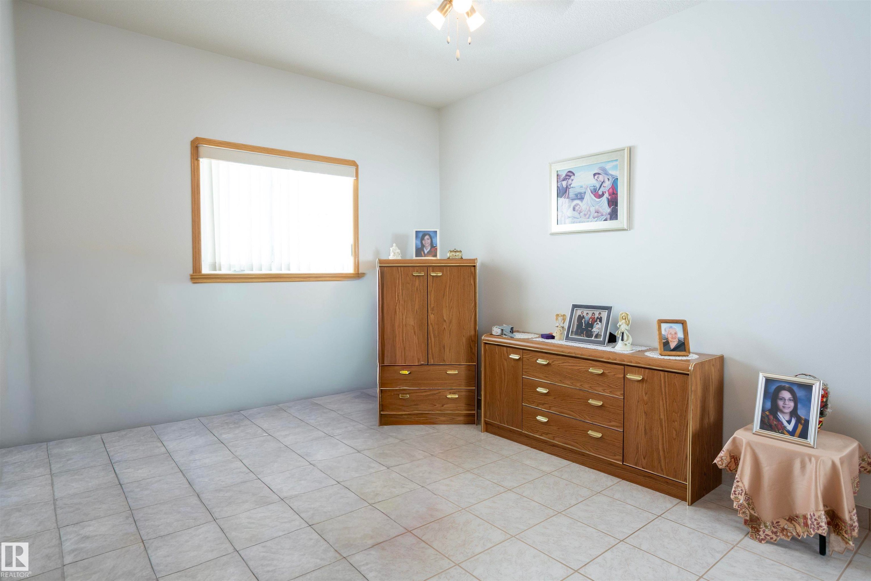 Spacious room featuring light-colored tile flooring, a window with wood trim, and a ceiling-mounted light fixture - 6407 163 Avenue Nw, Edmonton, AB