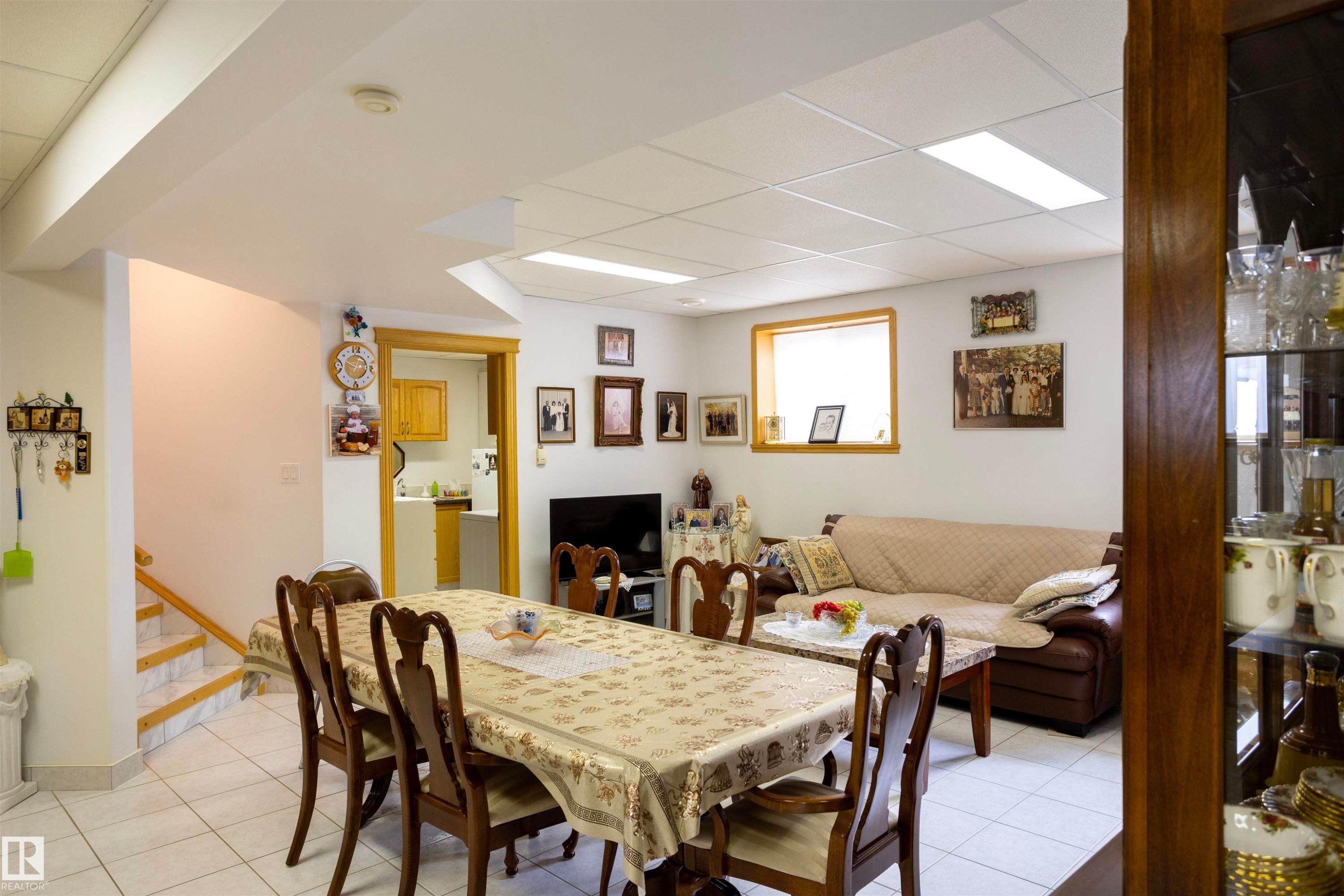 Spacious open-concept room featuring white tile flooring, a drop ceiling with integrated lighting, and white walls - 6407 163 Avenue Nw, Edmonton, AB