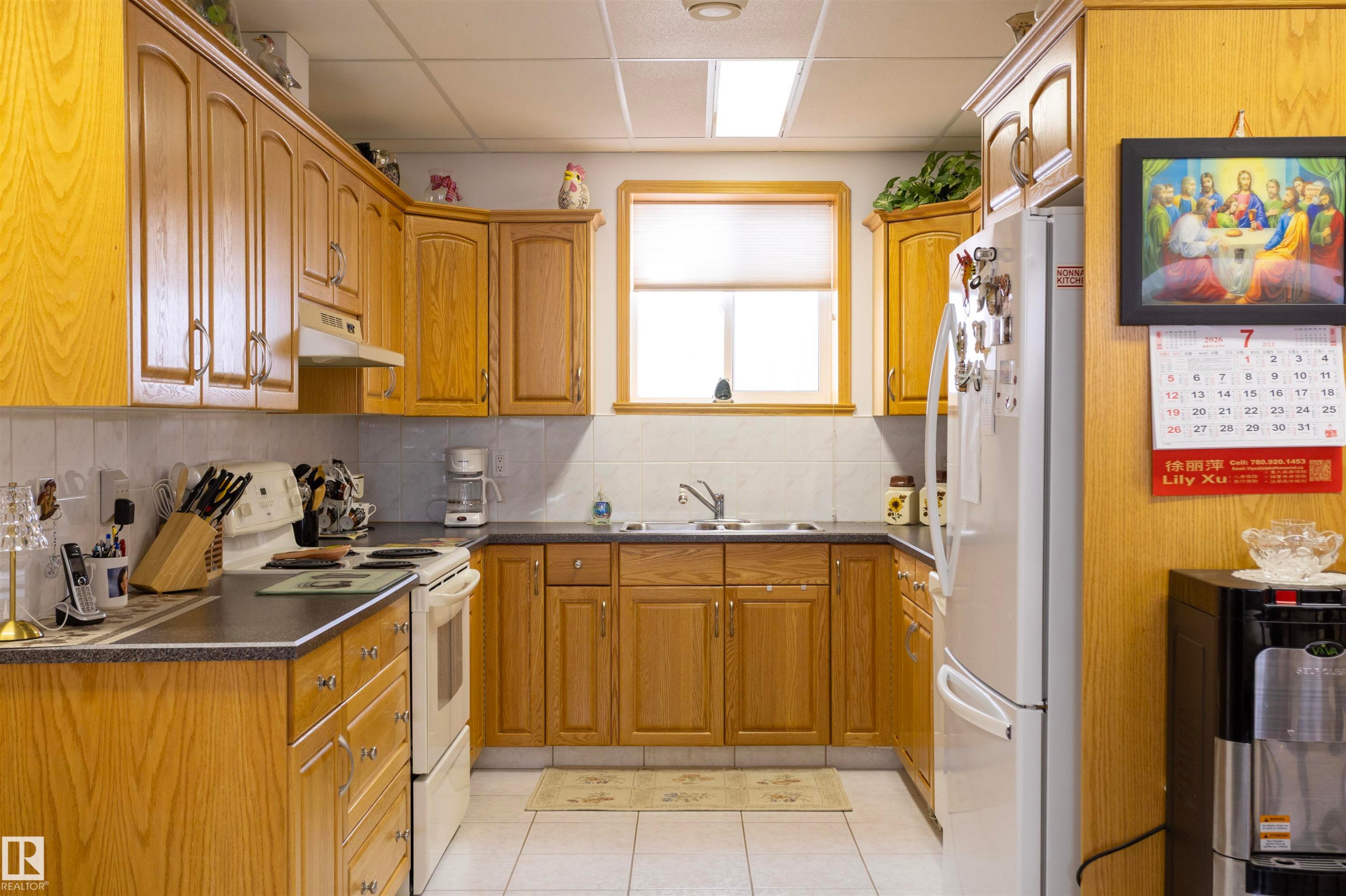 Kitchen featuring oak-finish cabinetry, dark countertops, white tile backsplash, and white tile flooring - 6407 163 Avenue Nw, Edmonton, AB