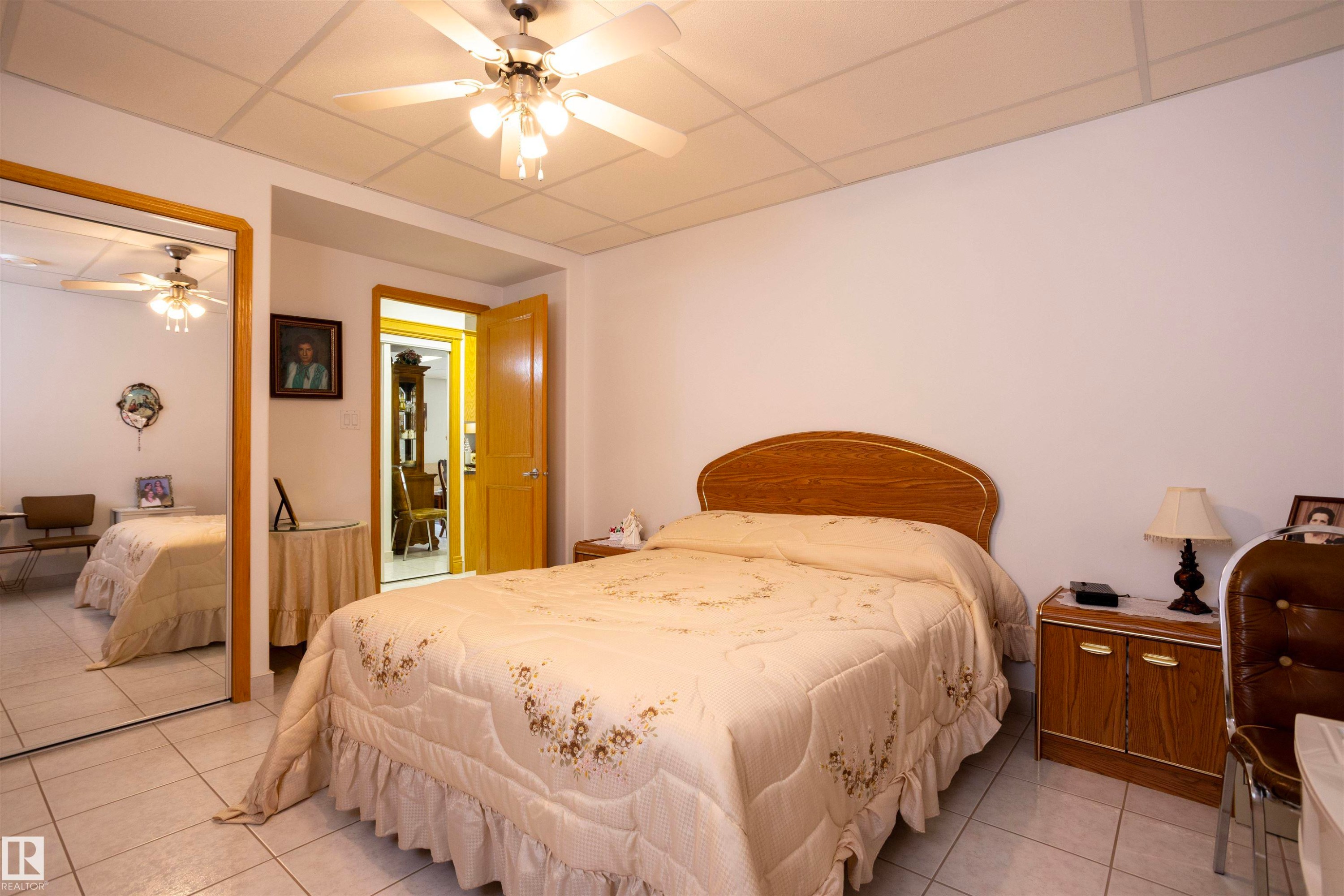 Bedroom featuring tile flooring, a built-in mirrored closet, a ceiling fan with integrated lighting, a solid core door, and a grid panel ceiling - 6407 163 Avenue Nw, Edmonton, AB