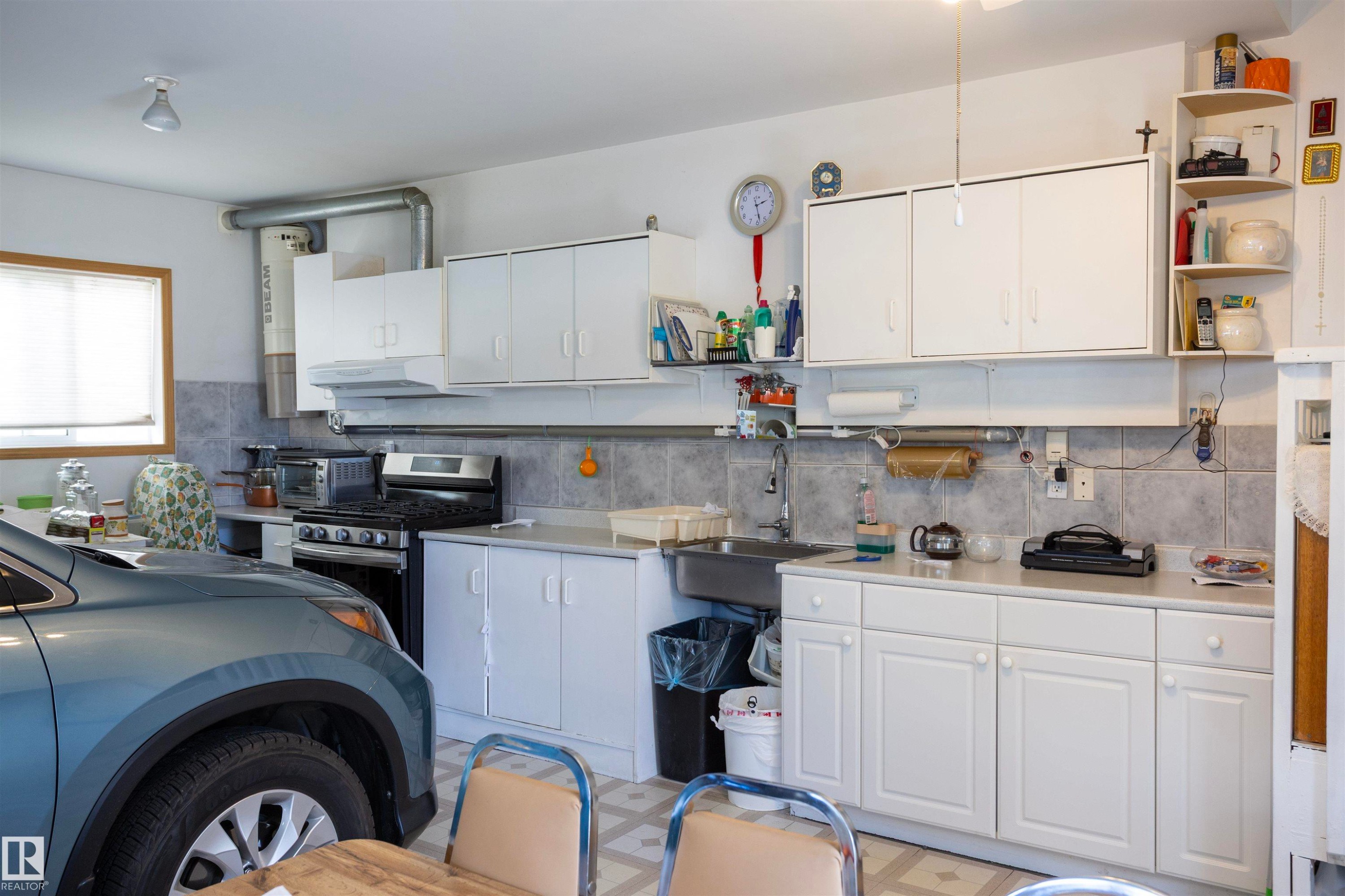 Garage space featuring extensive white cabinetry, a gas range, a stainless steel sink, tile backsplash, and a window for natural light - 6407 163 Avenue Nw, Edmonton, AB