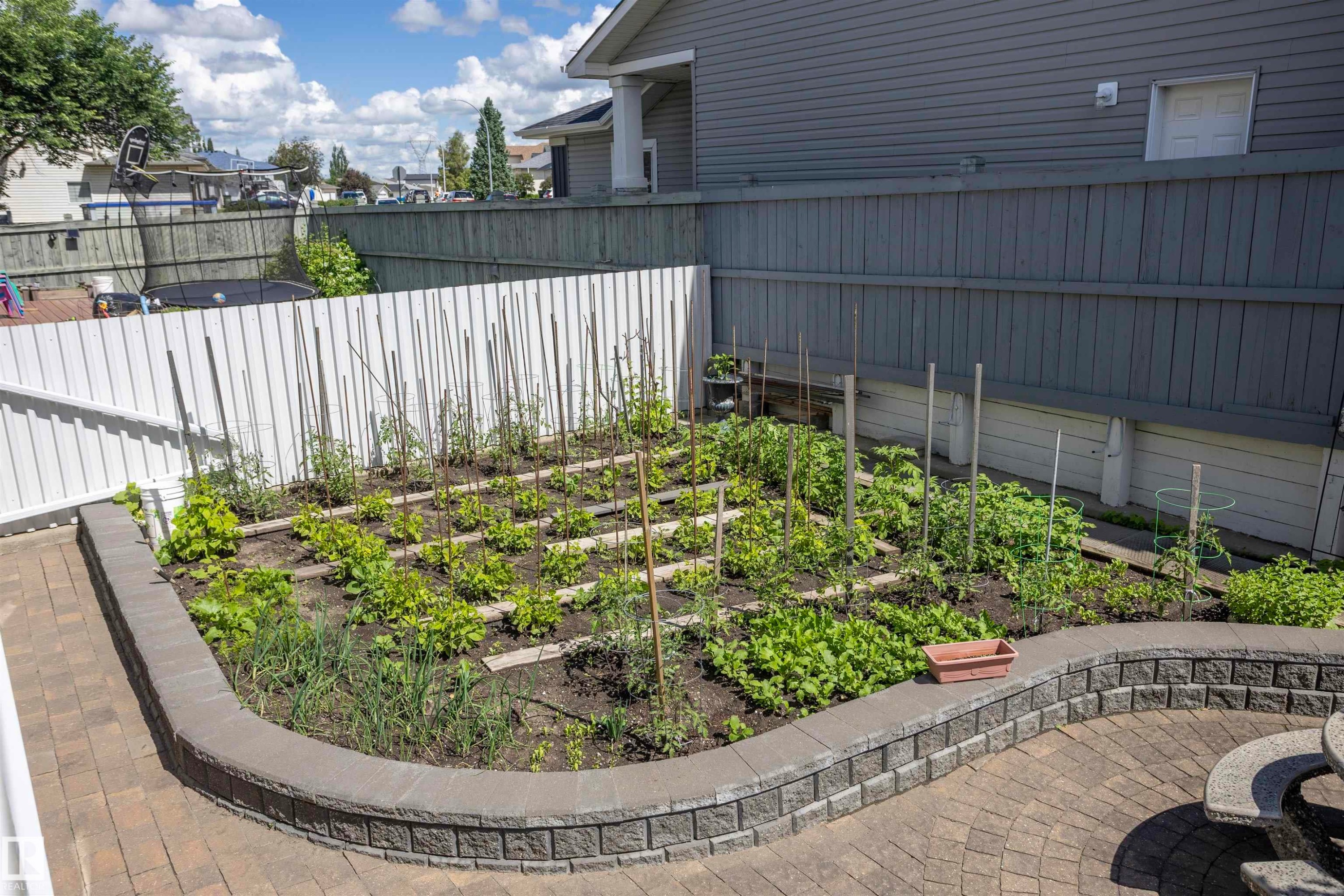 Paver patio with a curved stone retaining wall surrounding a garden bed - 6407 163 Avenue Nw, Edmonton, AB