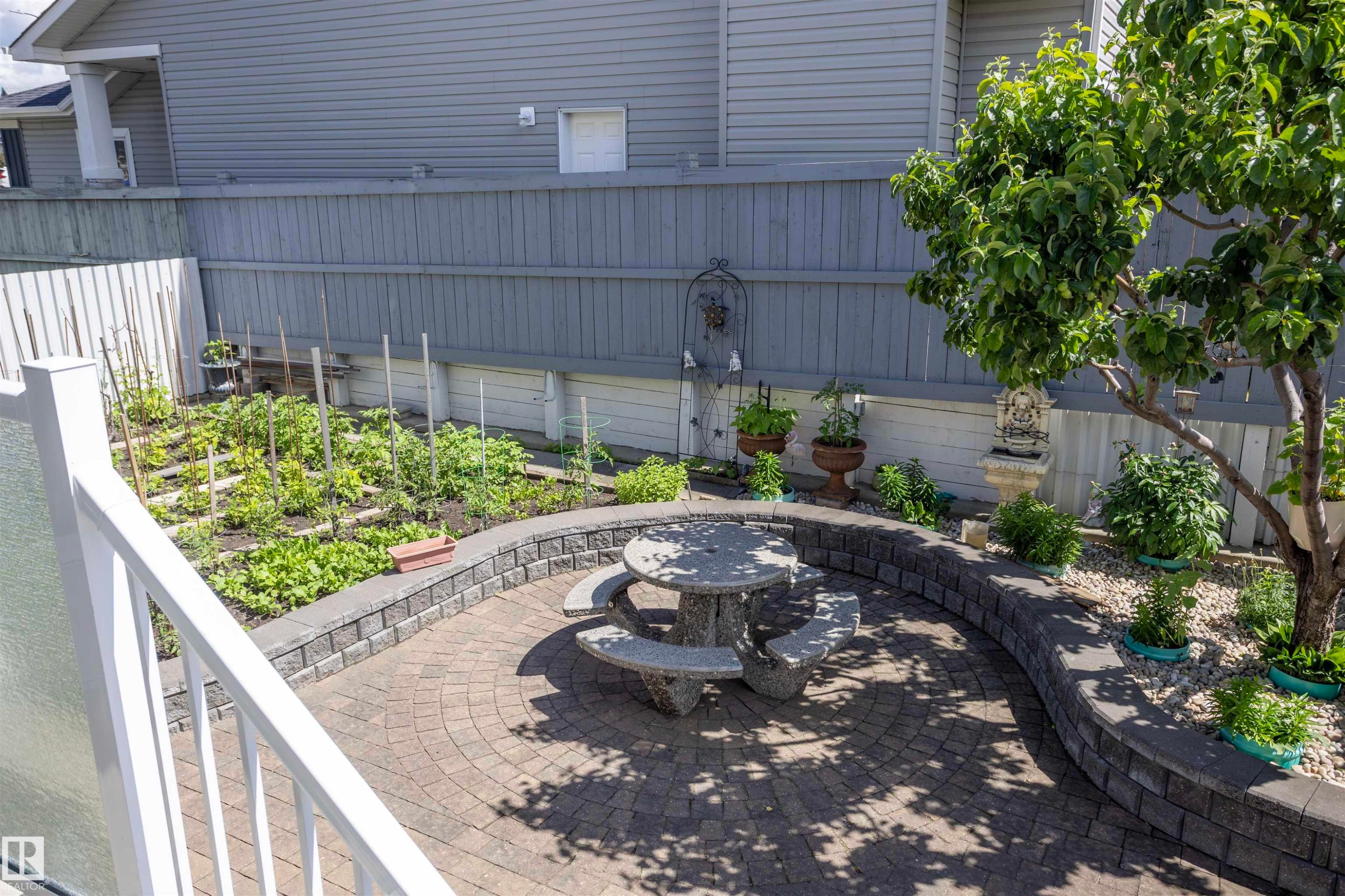 Spacious outdoor patio featuring a circular paver design, built-in block retaining walls, and a dedicated garden area - 6407 163 Avenue Nw, Edmonton, AB