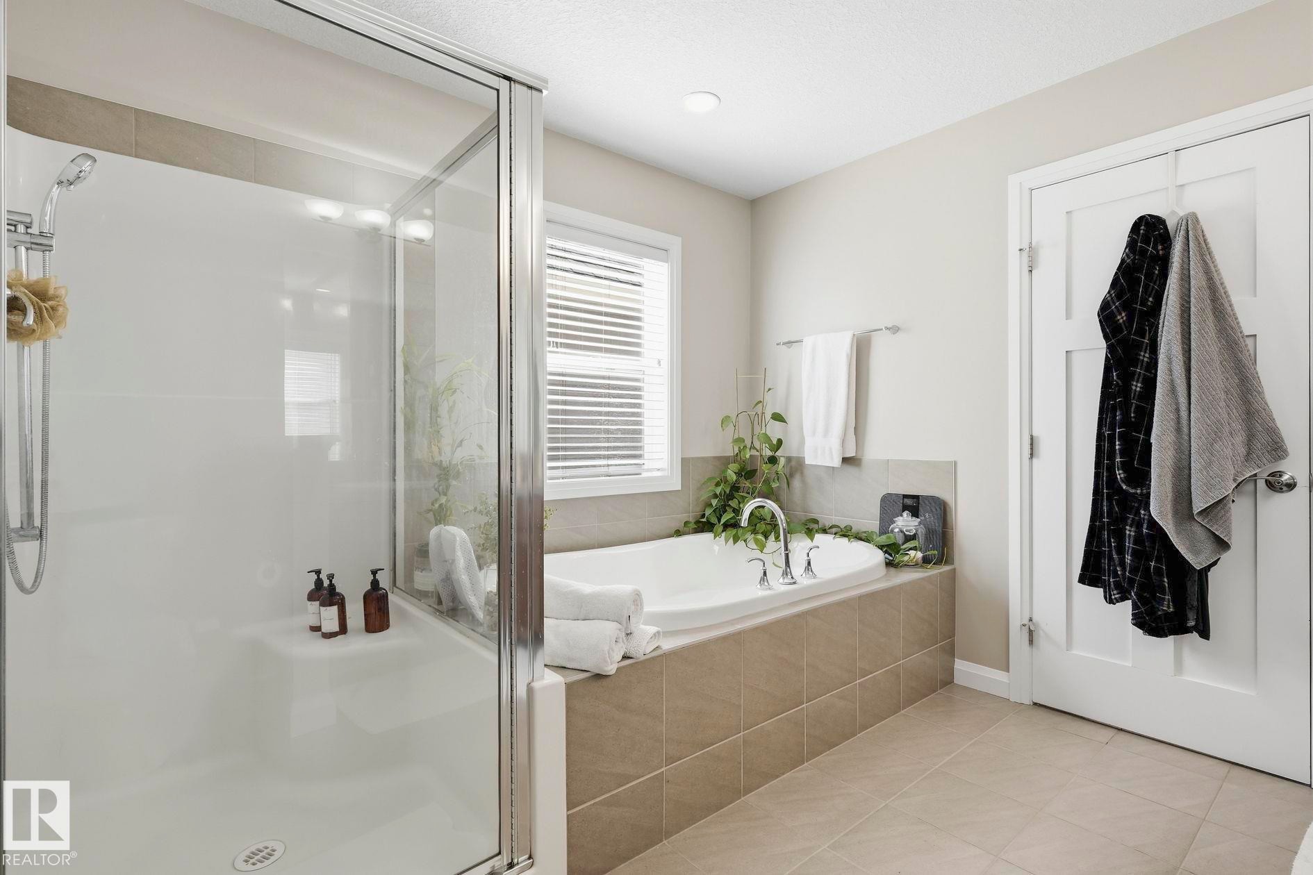 Bathroom featuring a tiled soaking tub surround, a built-in tub, a window with blinds, a glass-enclosed shower, and light-toned tile flooring - 3204 Abbott Crescent Sw, Edmonton, AB - Indoor Photo Showing Bathroom