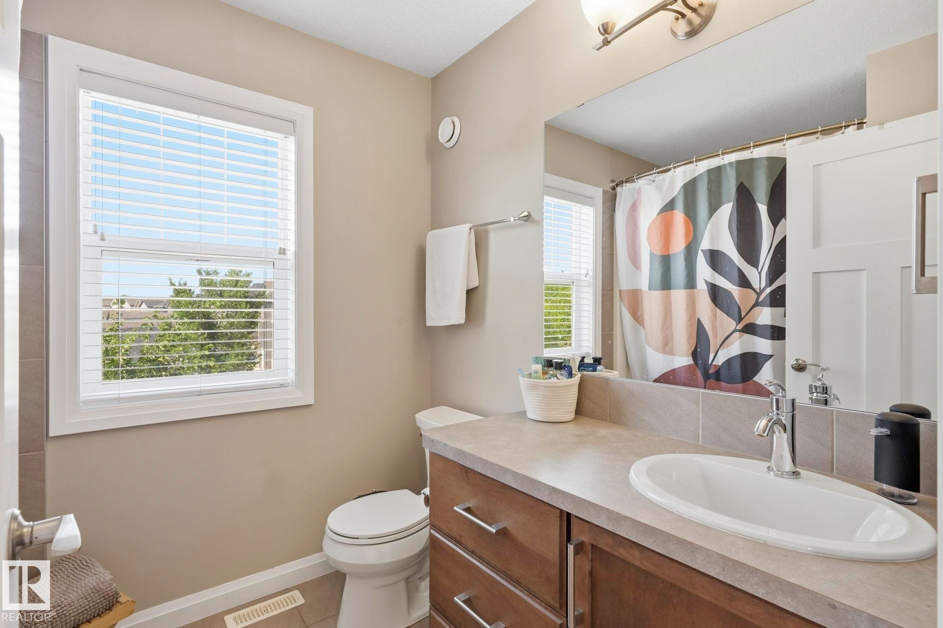 Bathroom featuring a wood-finish vanity with an integrated sink, a large mirror, and tiled flooring - 3204 Abbott Crescent Sw, Edmonton, AB - Indoor Photo Showing Bathroom