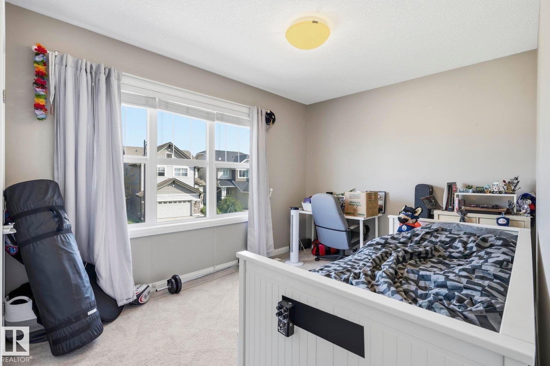 Bright bedroom featuring a large window with white trim, light gray carpet, and neutral wall paint - 3204 Abbott Crescent Sw, Edmonton, AB - Indoor