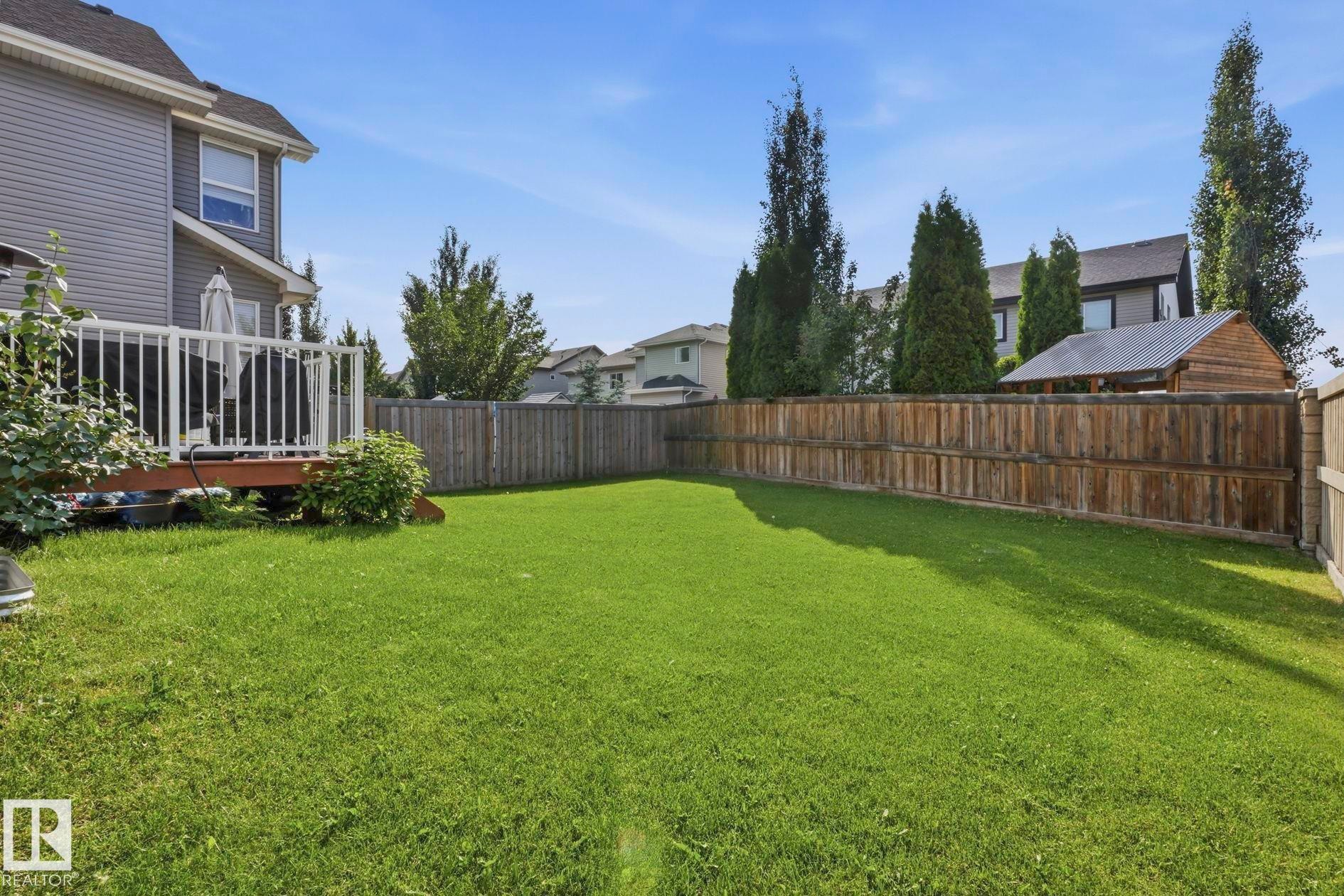 Expansive backyard featuring a lush lawn, a wood deck with white railings, and mature trees providing privacy - 3204 Abbott Crescent Sw, Edmonton, AB - Outdoor With Backyard