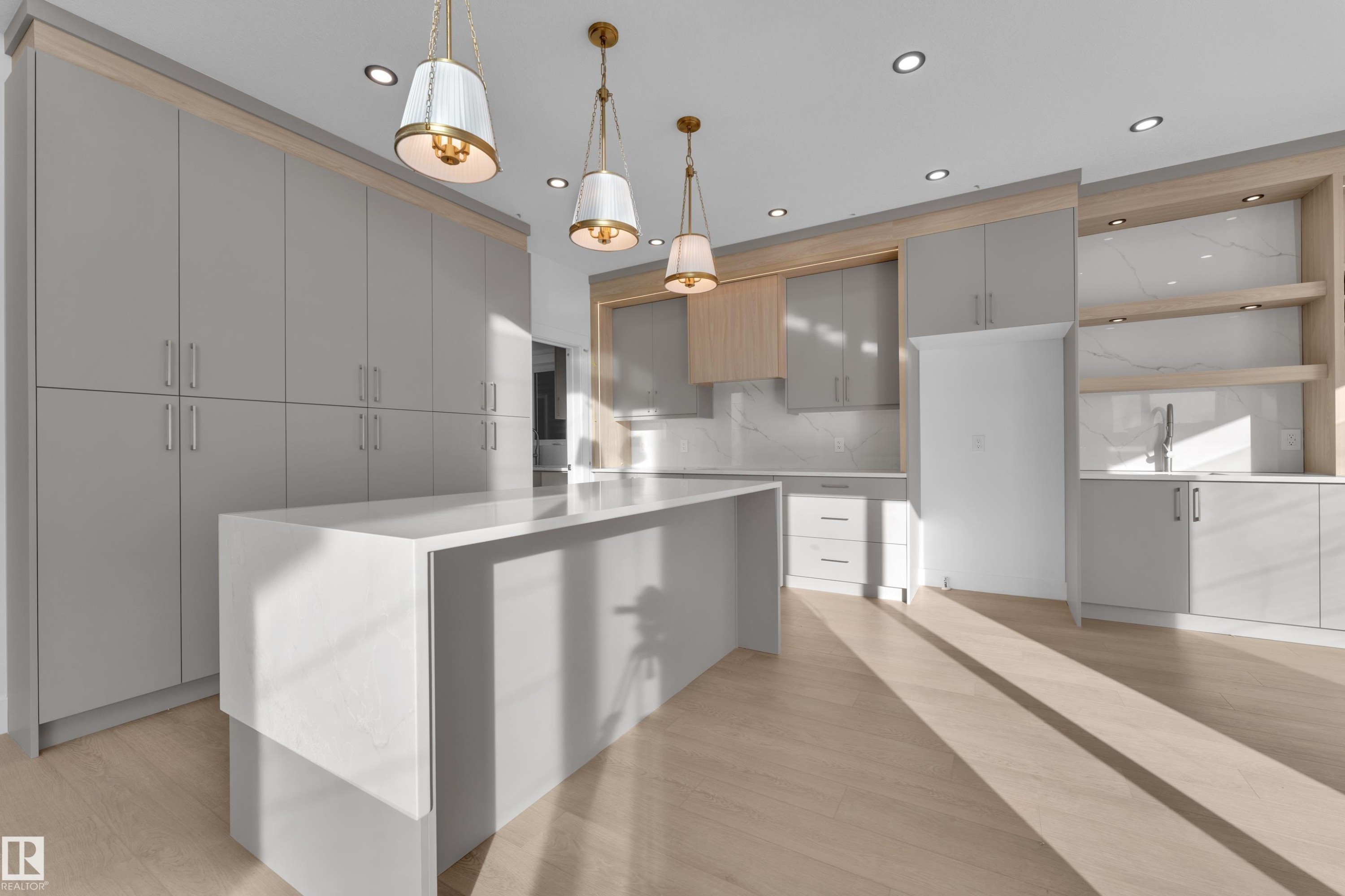 Spacious kitchen featuring an extended center island, wood-finish flooring, ample cabinetry, recessed lighting, and elegant pendant light fixtures - 226 Linden Loop, Leduc, AB