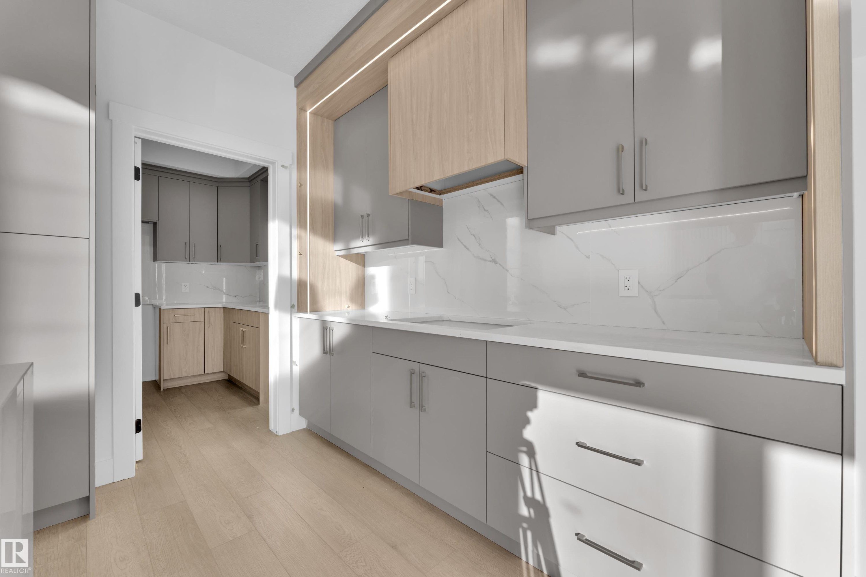 Modern kitchen featuring light wood-finish flooring, two-tone cabinetry with sleek hardware, white countertop, and a marble-patterned backsplash - 226 Linden Loop, Leduc, AB