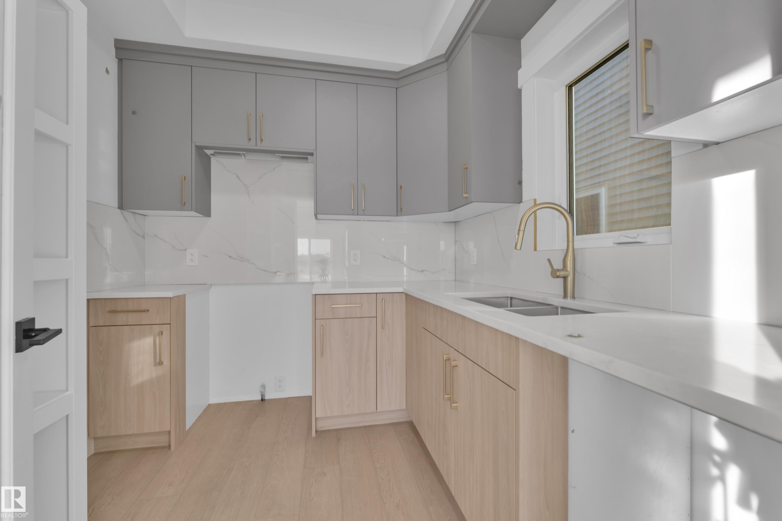 Kitchen featuring light gray upper cabinetry, natural wood-finish lower cabinetry, white countertops, a dual basin stainless steel sink, and a gold-tone gooseneck faucet - 226 Linden Loop, Leduc, AB