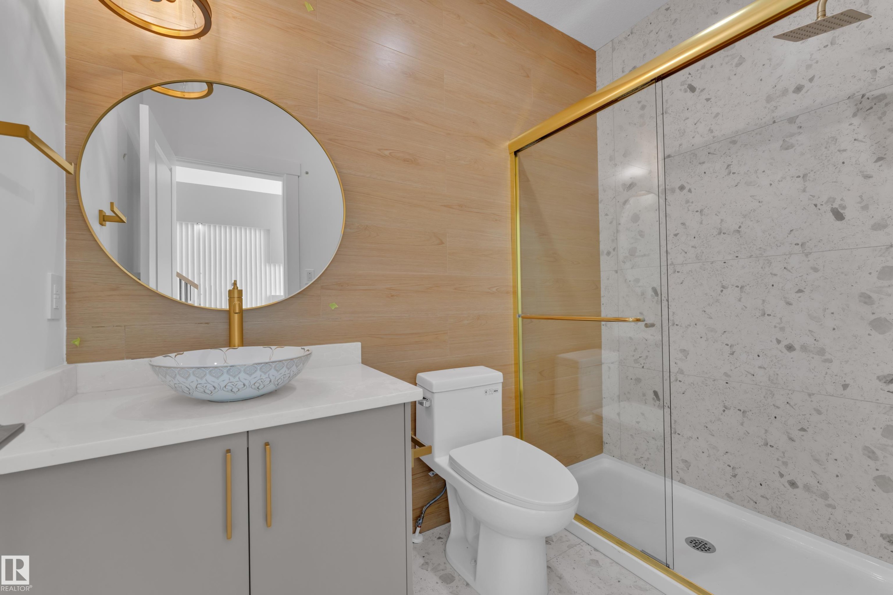 Modern vanity with a vessel sink, gold-finish fixtures, a gold-framed round mirror, and a shower with a sliding glass door - 226 Linden Loop, Leduc, AB