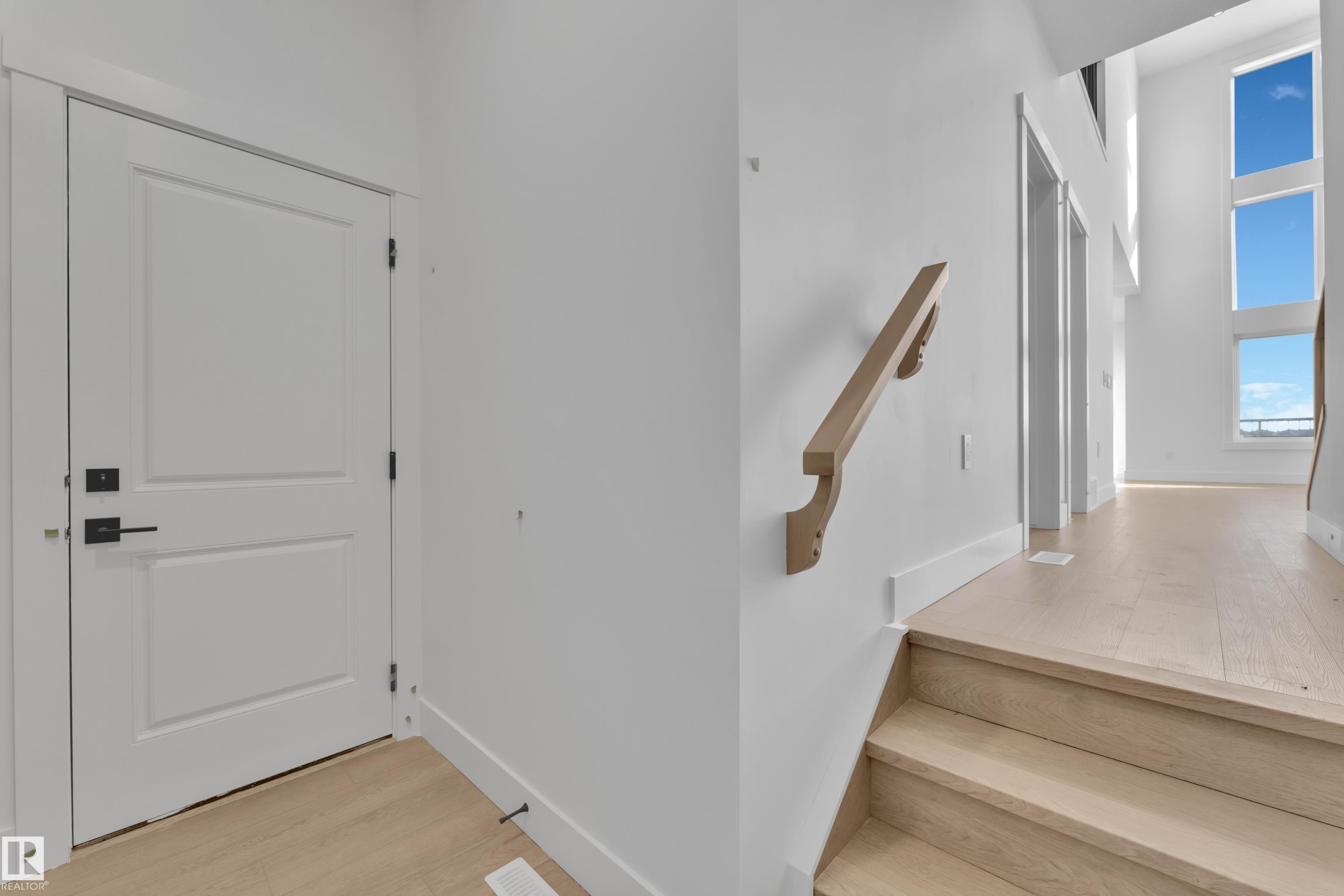 Vertical windows, light wood-finish flooring, white paneled door, and a natural wood handrail - 226 Linden Loop, Leduc, AB