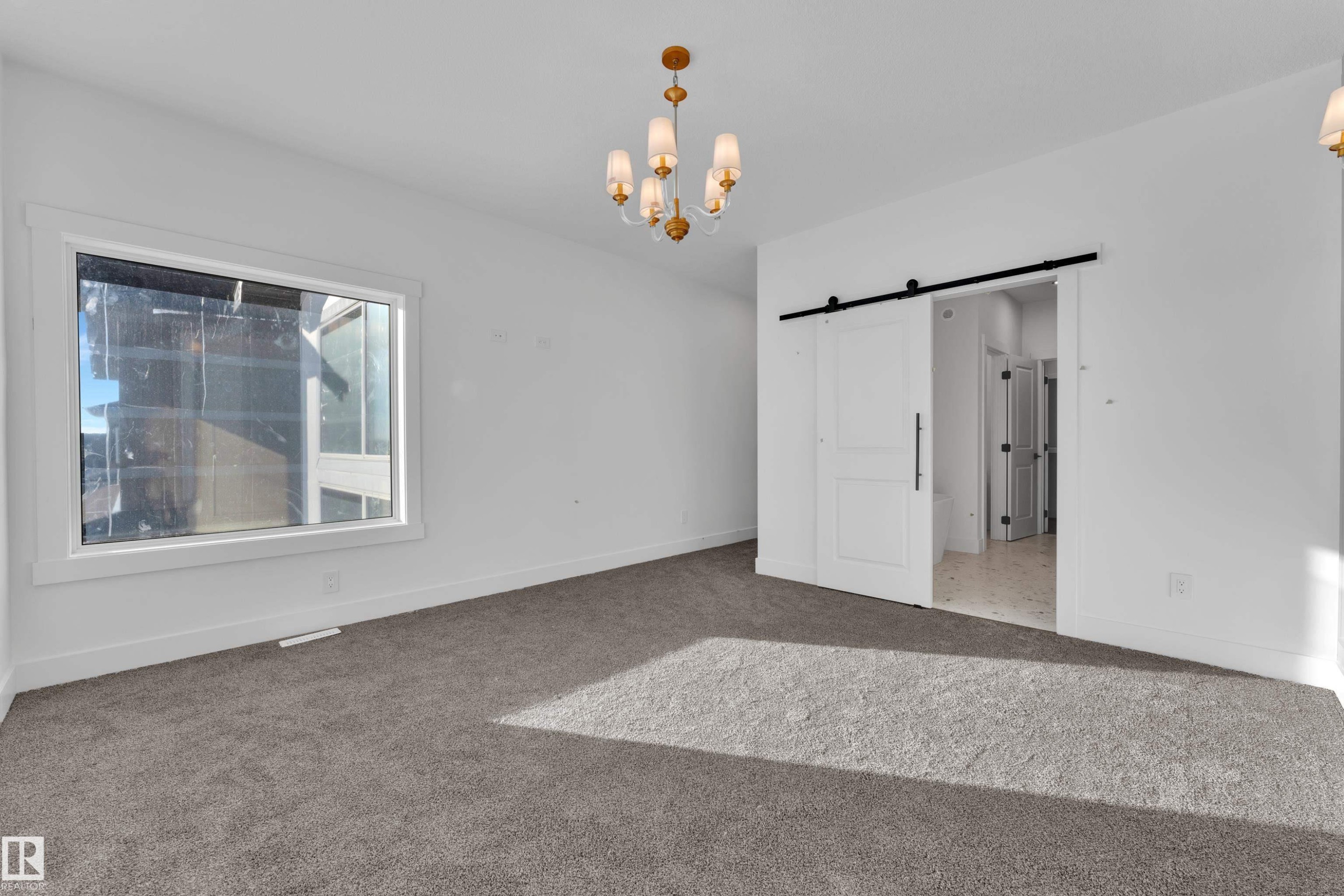 Spacious room featuring a large window, neutral carpeting, and a stylish chandelier - 226 Linden Loop, Leduc, AB