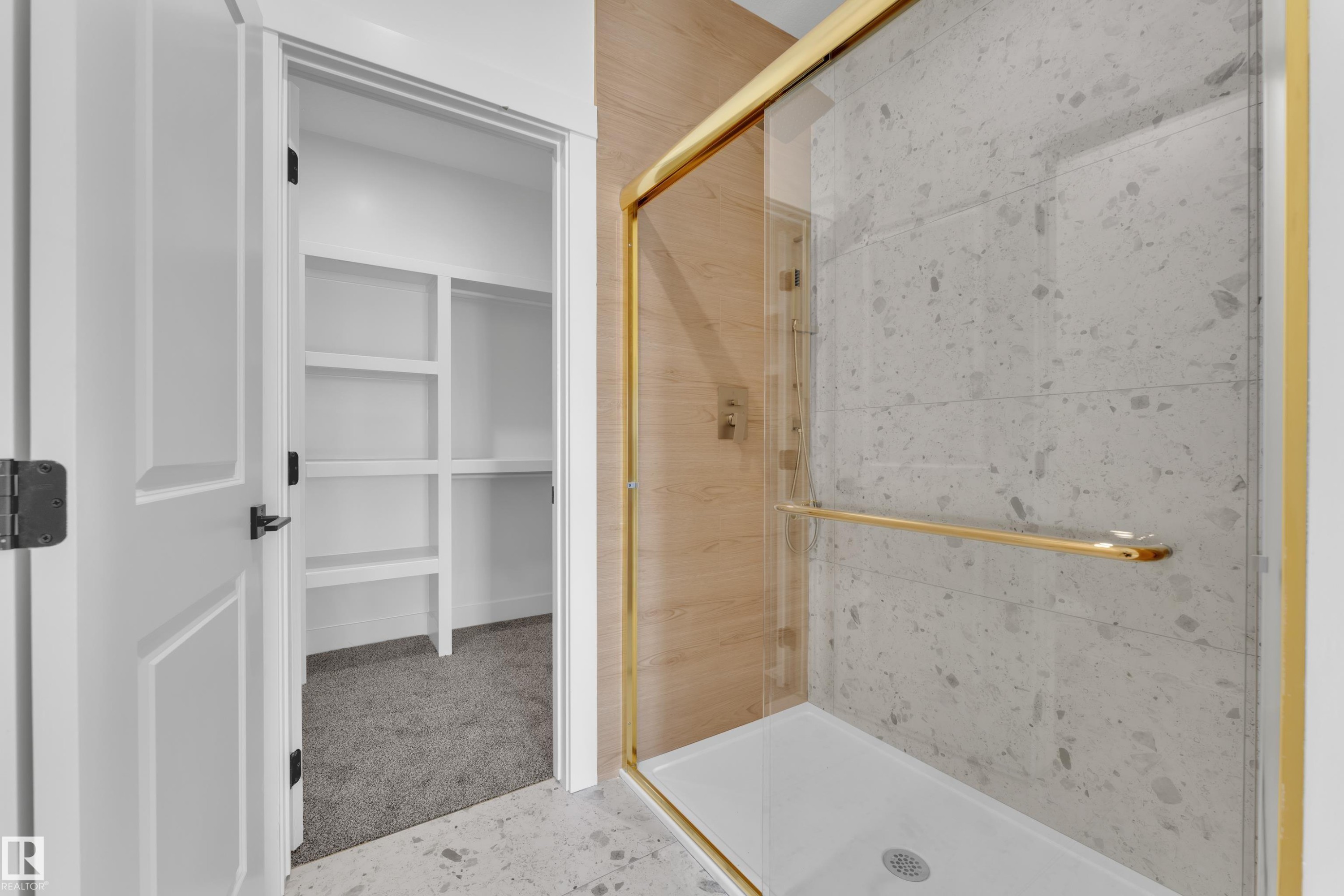 Walk-in shower with gold-toned frame and hardware, large-format tile surround, and built-in shelving in an adjacent closet - 226 Linden Loop, Leduc, AB