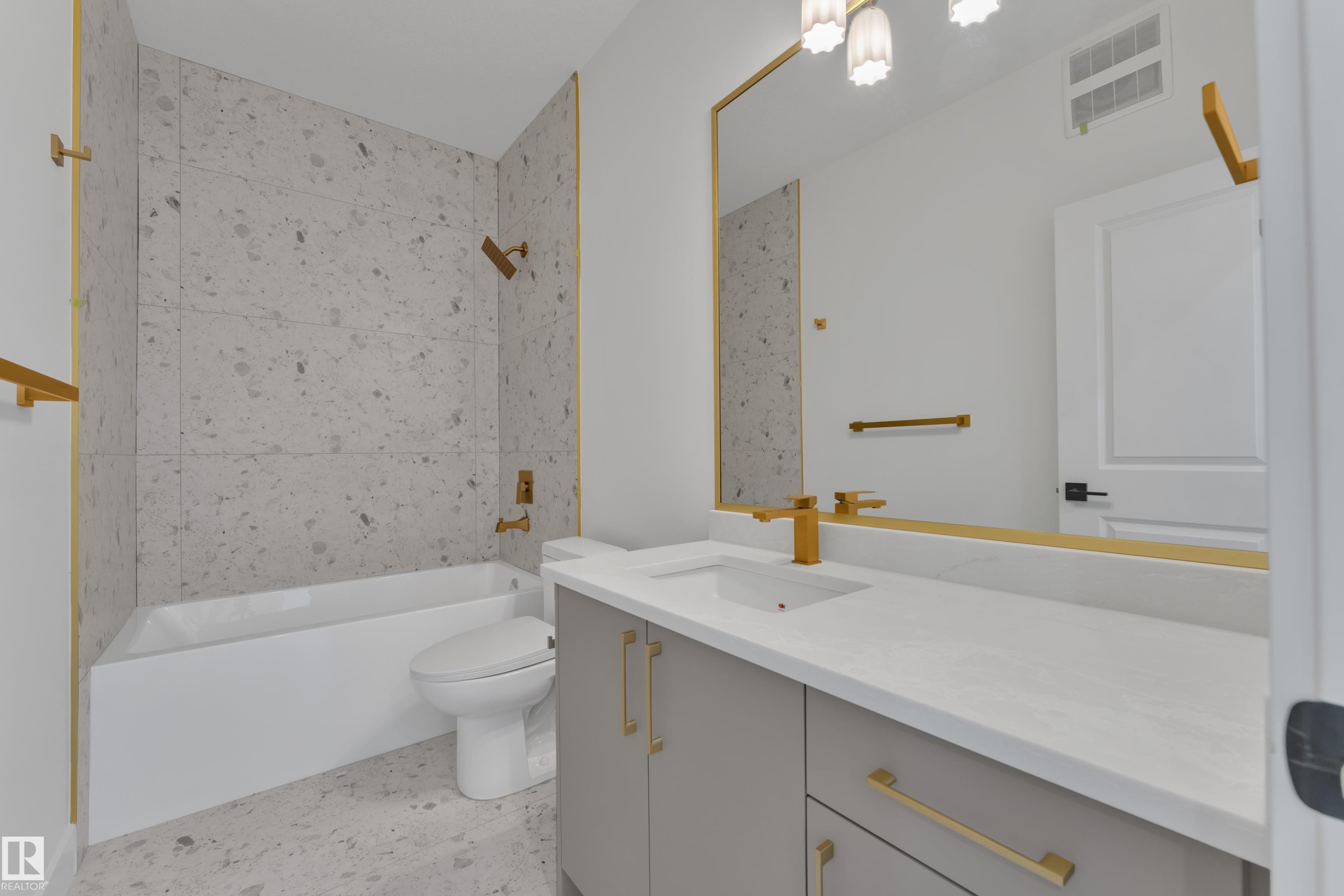 Bathroom featuring a built-in tub with tile surround, a single vanity with an undermount sink, a large mirror with a gold-tone frame, and gold-tone fixtures - 226 Linden Loop, Leduc, AB
