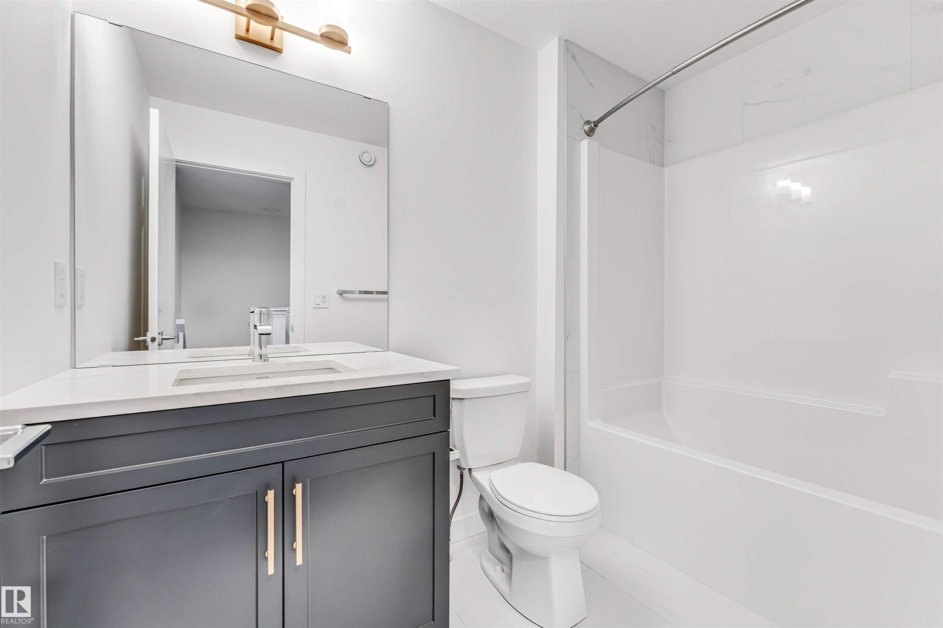 Dark gray vanity with brass-finish hardware, rectangular undermount sink, quartz countertop, and large wall mirror - #48 710 Mattson Dr Sw Sw, Edmonton, AB