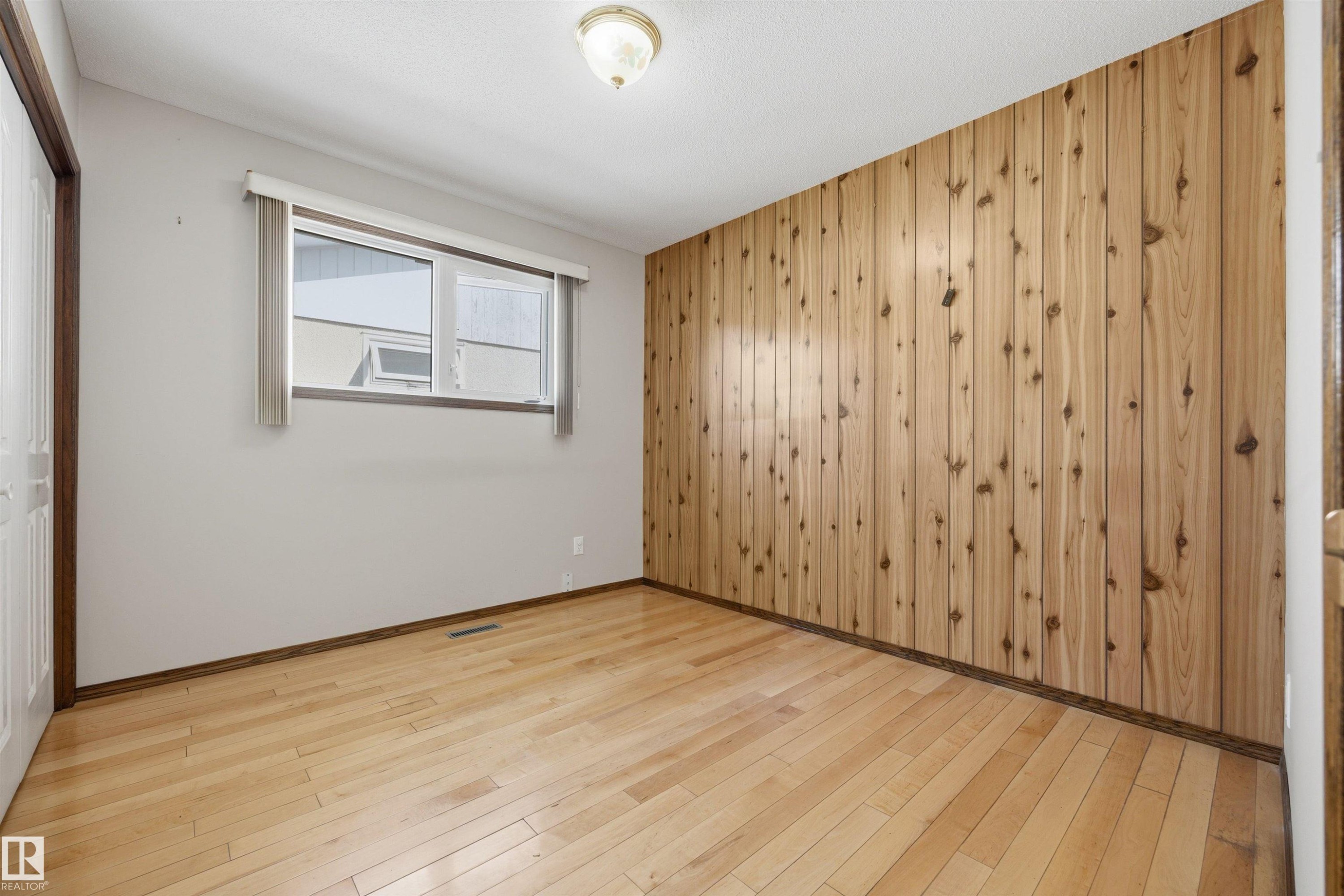 Wood-finish flooring, paneled wood accent wall, and a window with blinds - 14008 94 Street Nw, Edmonton, AB