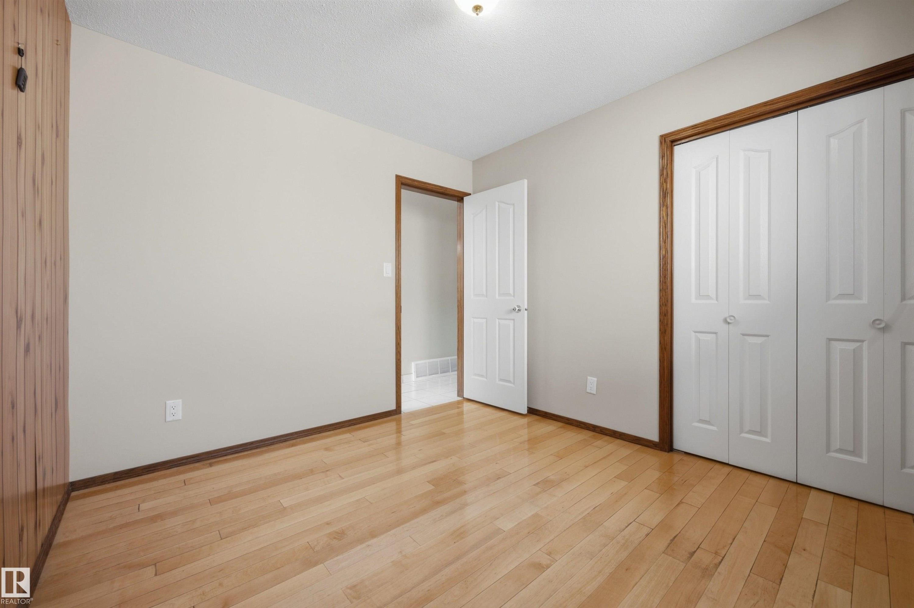 Hardwood flooring, painted walls, bi-fold closet doors, wood-paneled wall, and contrasting wood trim - 14008 94 Street Nw, Edmonton, AB