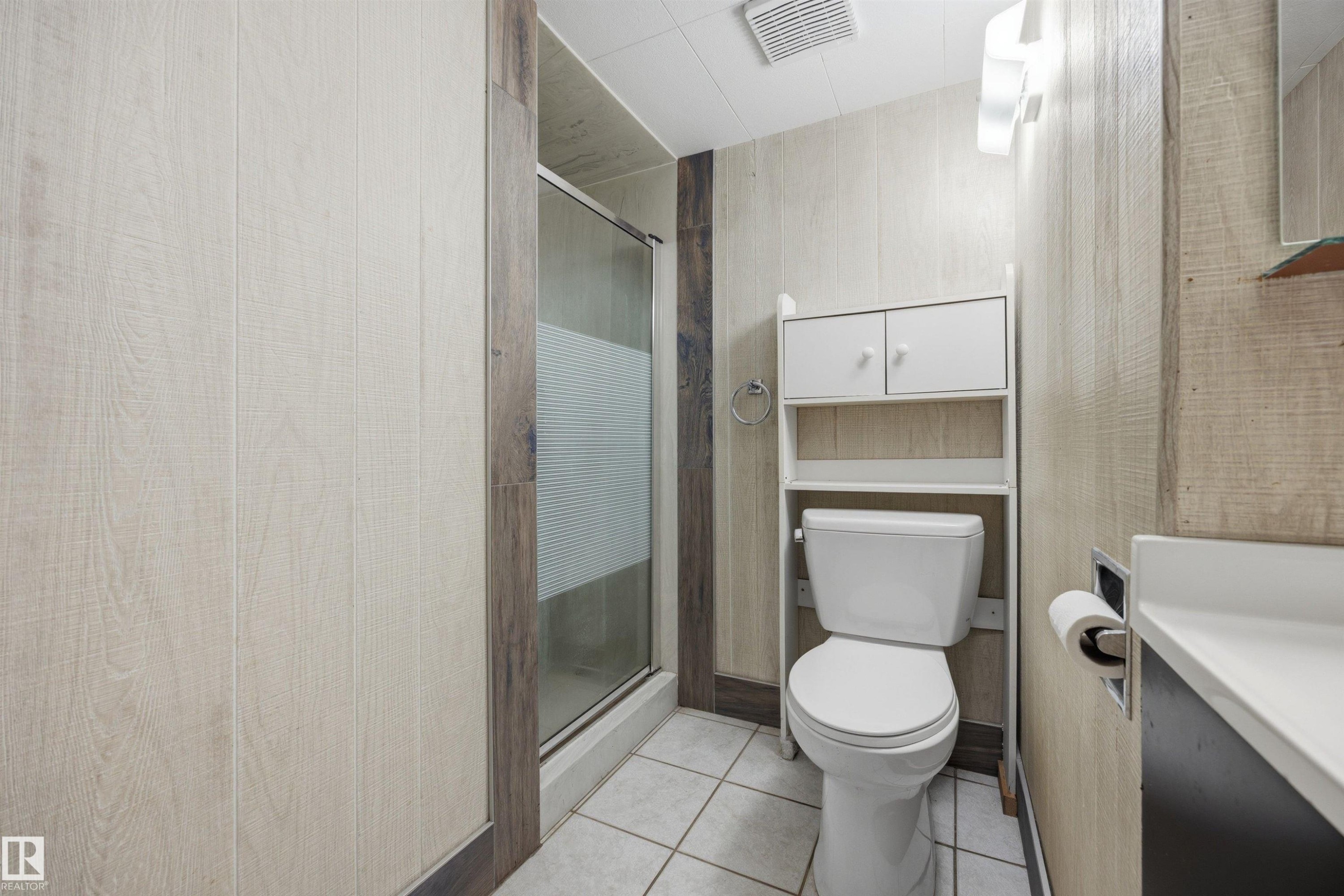 Shower enclosure with glass door, wall-mounted vanity with integrated sink, white toilet, and overhead storage cabinetry - 14008 94 Street Nw, Edmonton, AB