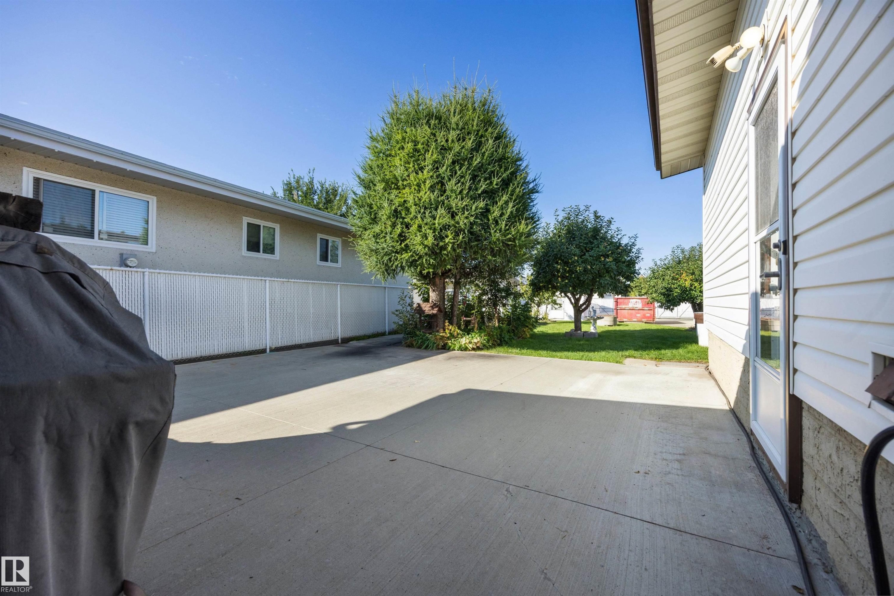 Concrete patio with a rear entry door, white vinyl siding, and a chain-link fence - 14008 94 Street Nw, Edmonton, AB