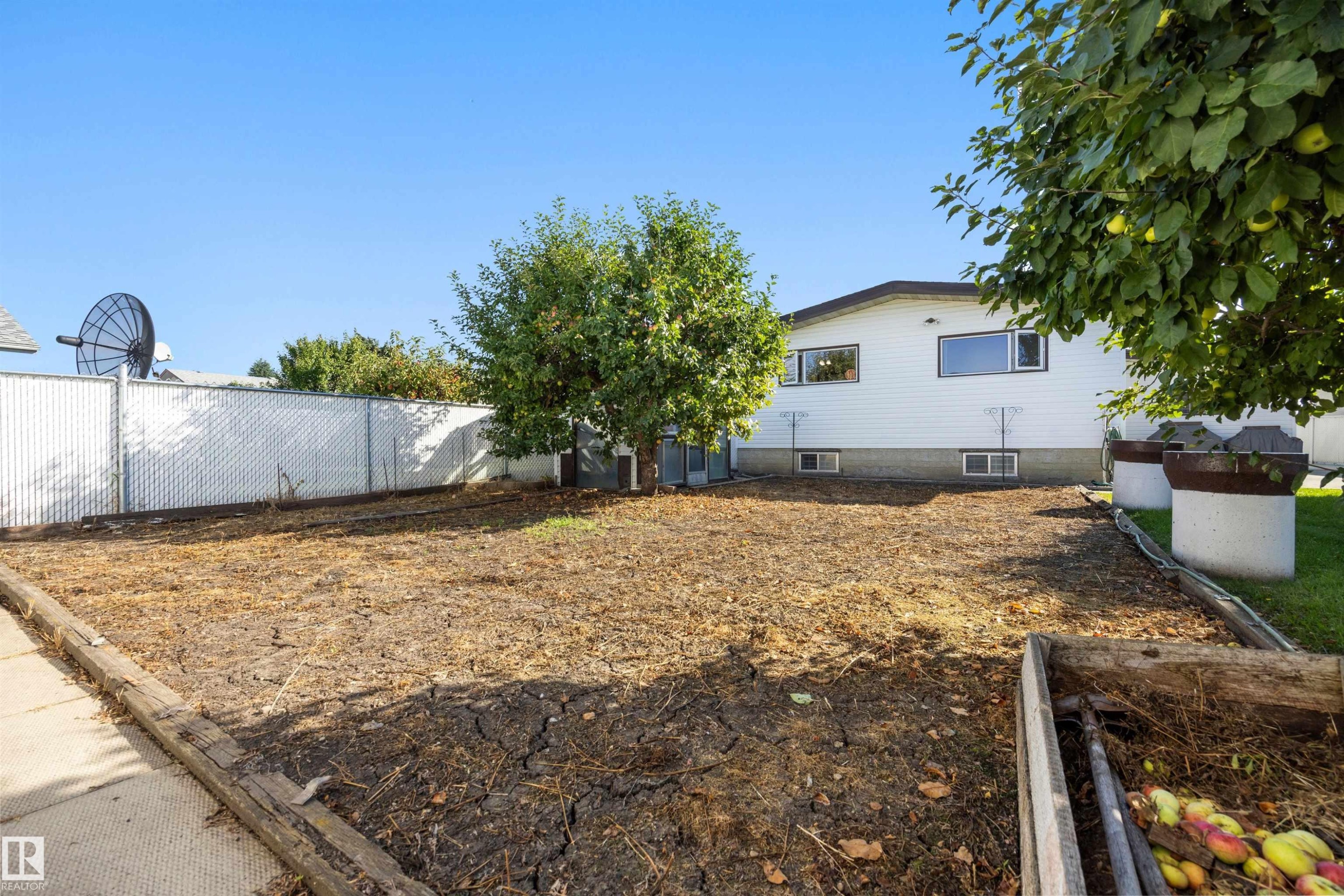 Fenced backyard featuring mature trees, a concrete walkway, and a raised garden bed - 14008 94 Street Nw, Edmonton, AB