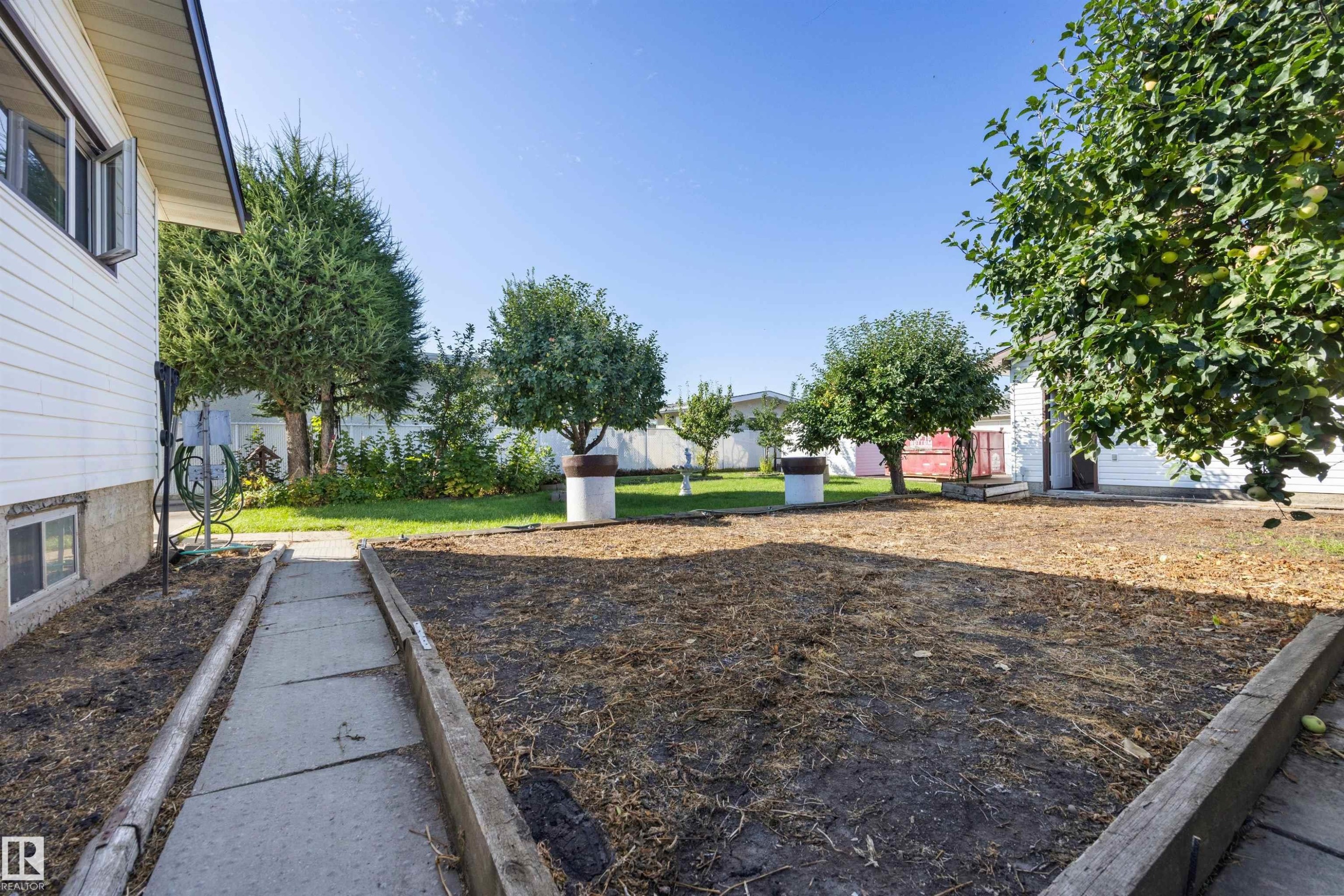 Expansive backyard with a concrete pathway, mature trees, and a garden bed - 14008 94 Street Nw, Edmonton, AB