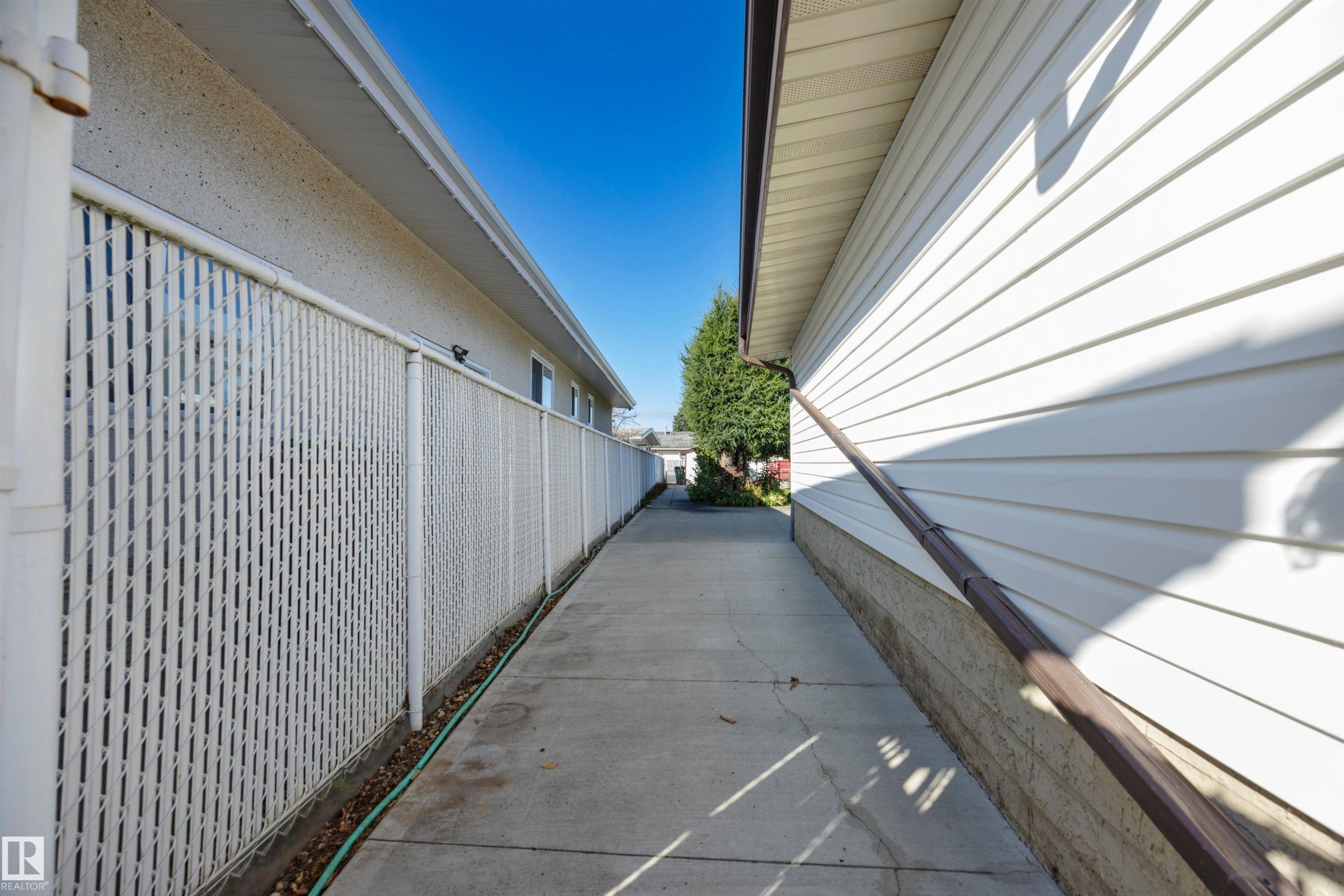Concrete pathway with a chain-link fence, white vinyl siding, and brown eavestroughs - 14008 94 Street Nw, Edmonton, AB