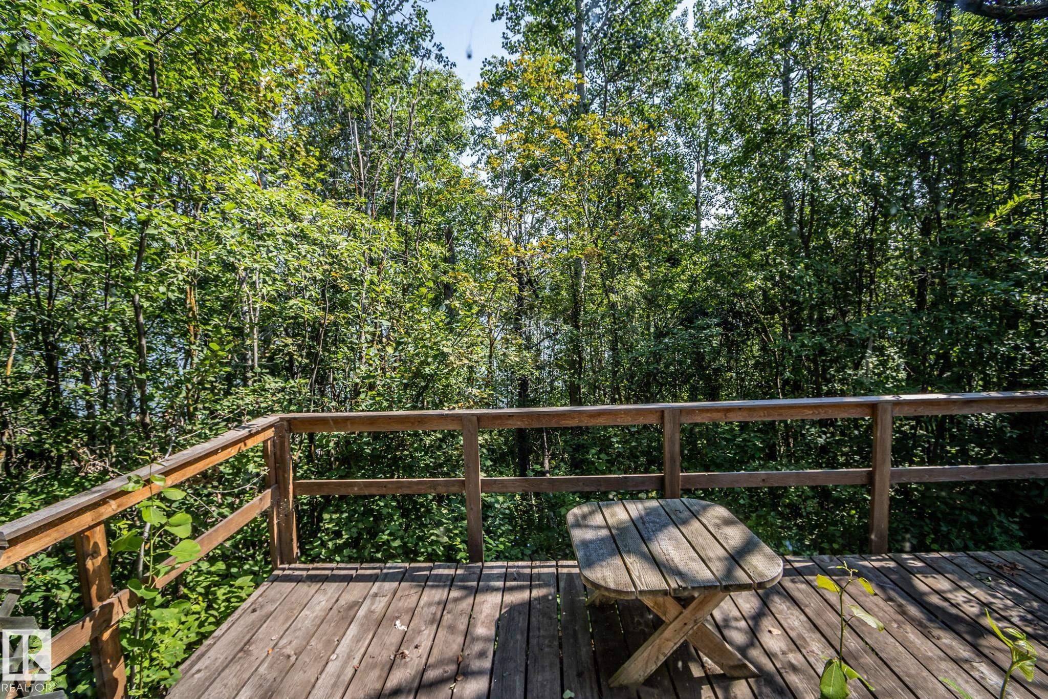 Wood deck with a natural wood railing, surrounded by mature trees - 811 59209 Range Rd 95A, Rural St. Paul County, AB - Outdoor With Deck Patio Veranda