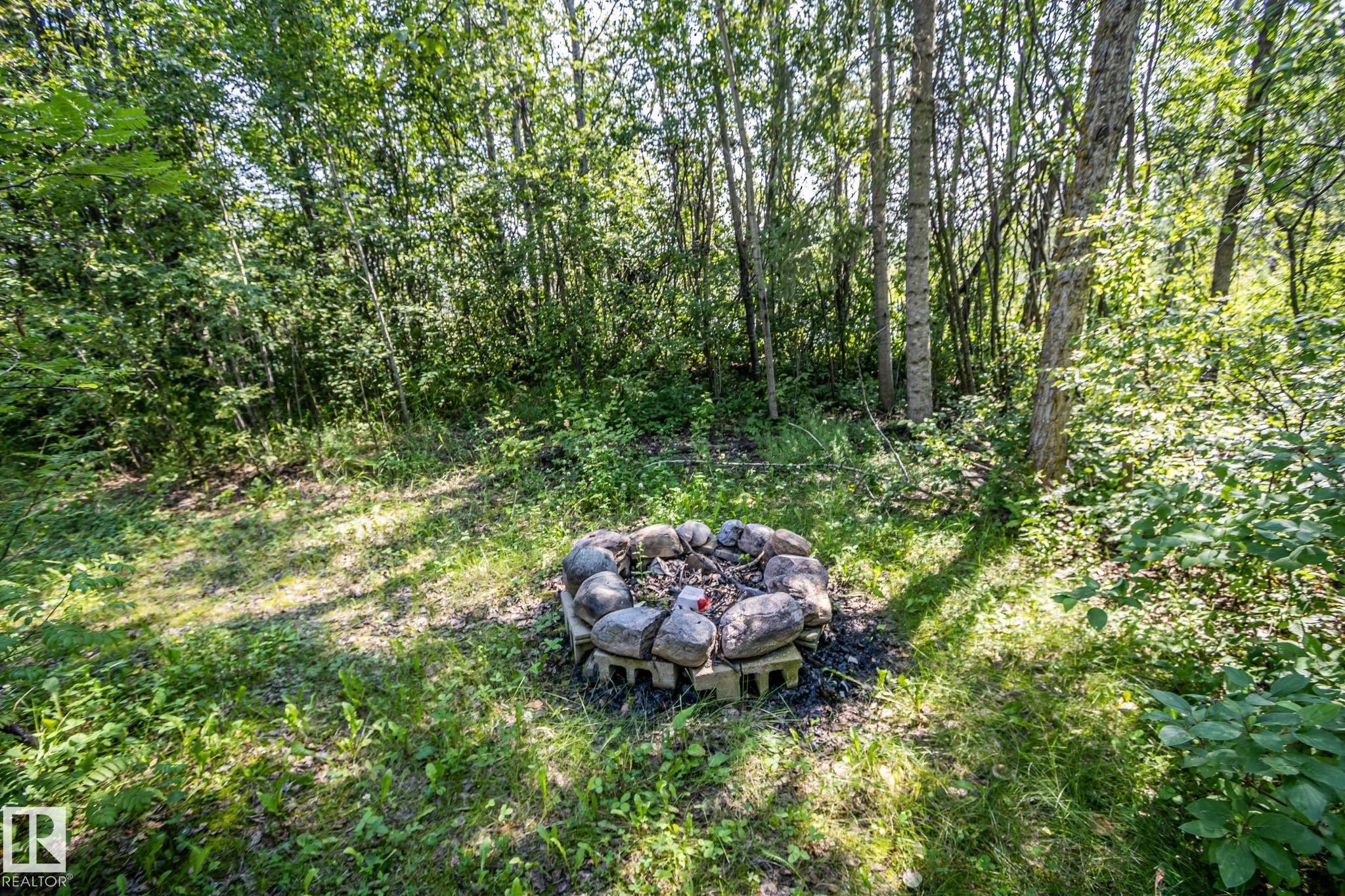 Outdoor fire pit with natural stone surround and a wooded backdrop - 811 59209 Range Rd 95A, Rural St. Paul County, AB - Outdoor