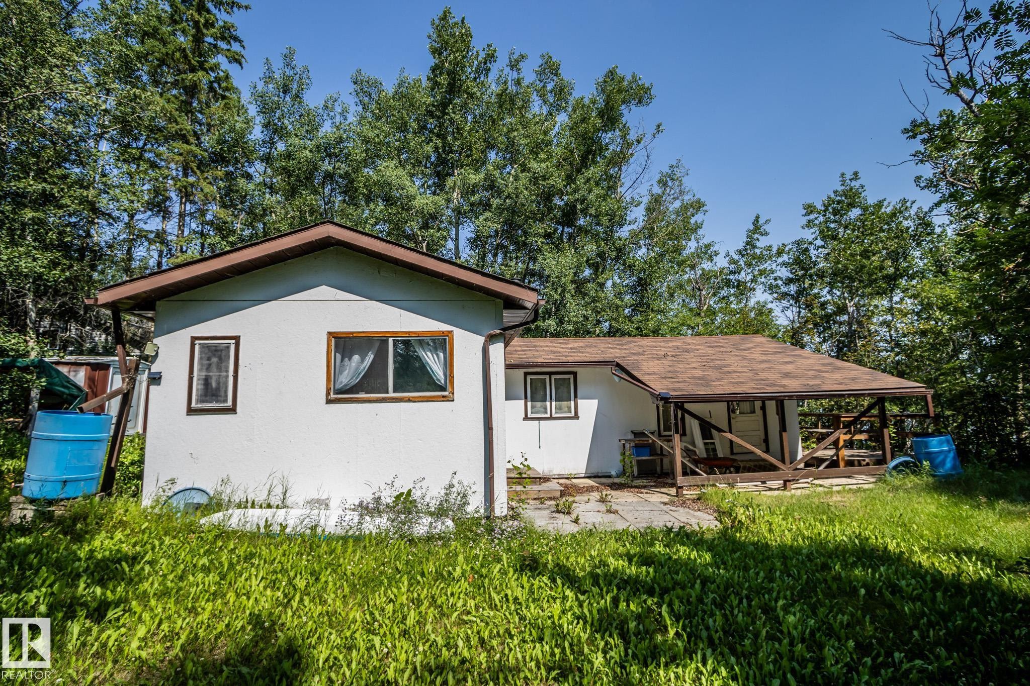 White exterior residence featuring a brown shingle roof, wood-frame windows, and a covered porch - 811 59209 Range Rd 95A, Rural St. Paul County, AB - Outdoor
