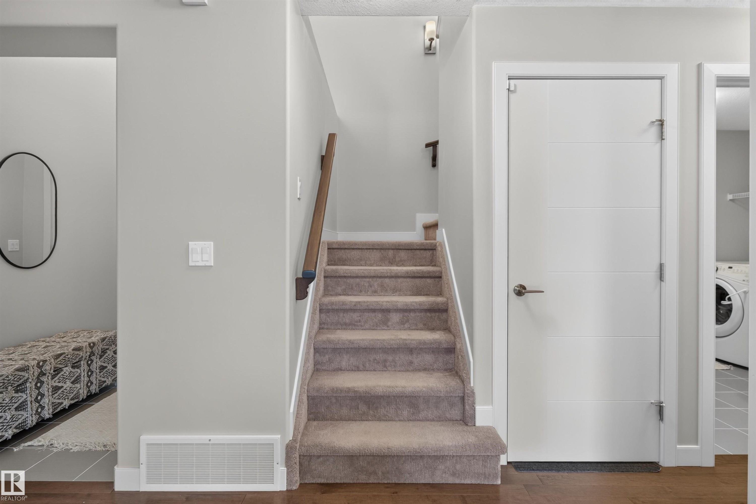 Wood-finish flooring, carpeted staircase with wood handrail, paneled interior door, and a built-in washer and dryer visible in the background - 5130 Godson Close Nw, Edmonton, AB