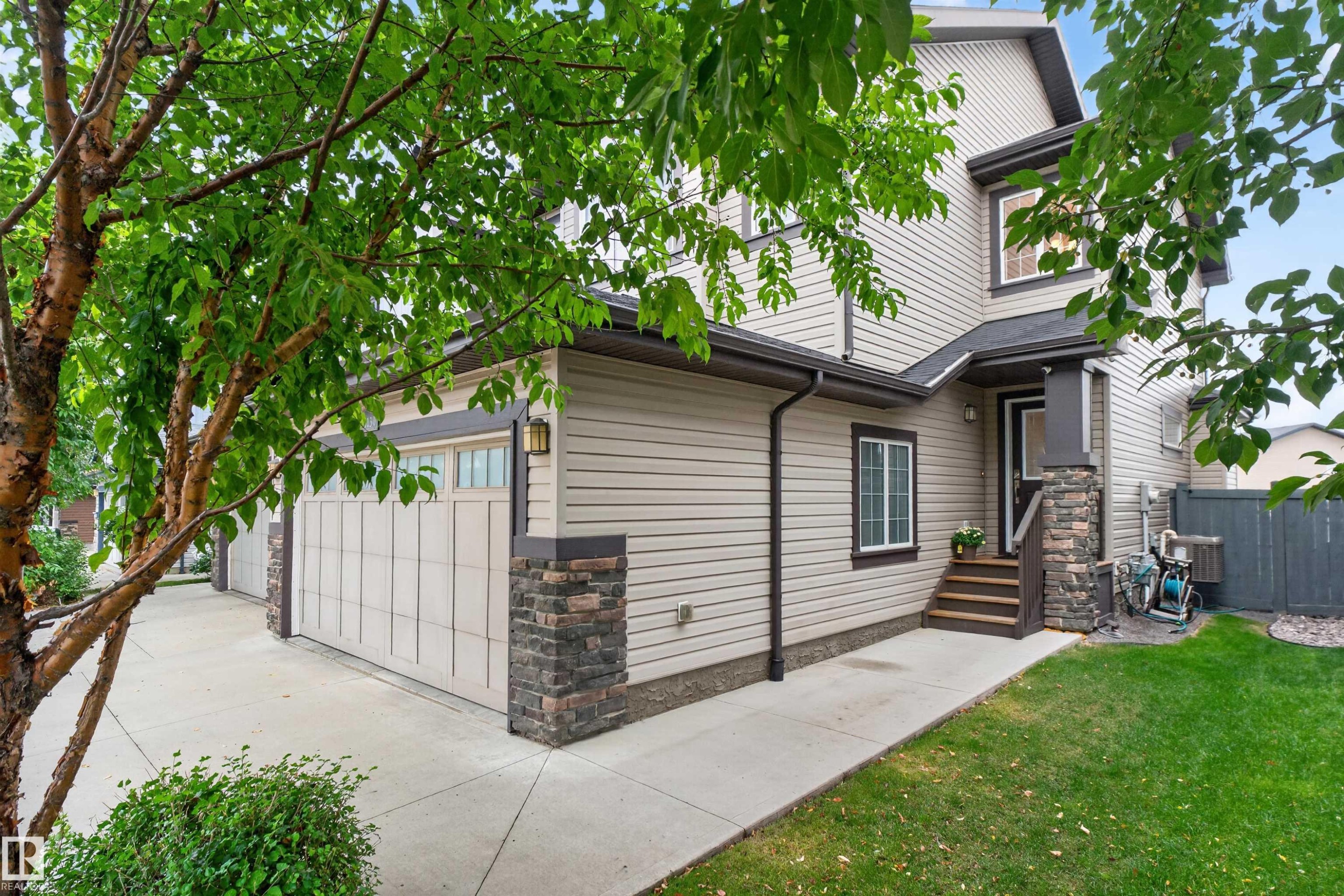 Two-story exterior with light-toned siding, stone accents, concrete driveway, and a covered entry - 5130 Godson Close Nw, Edmonton, AB