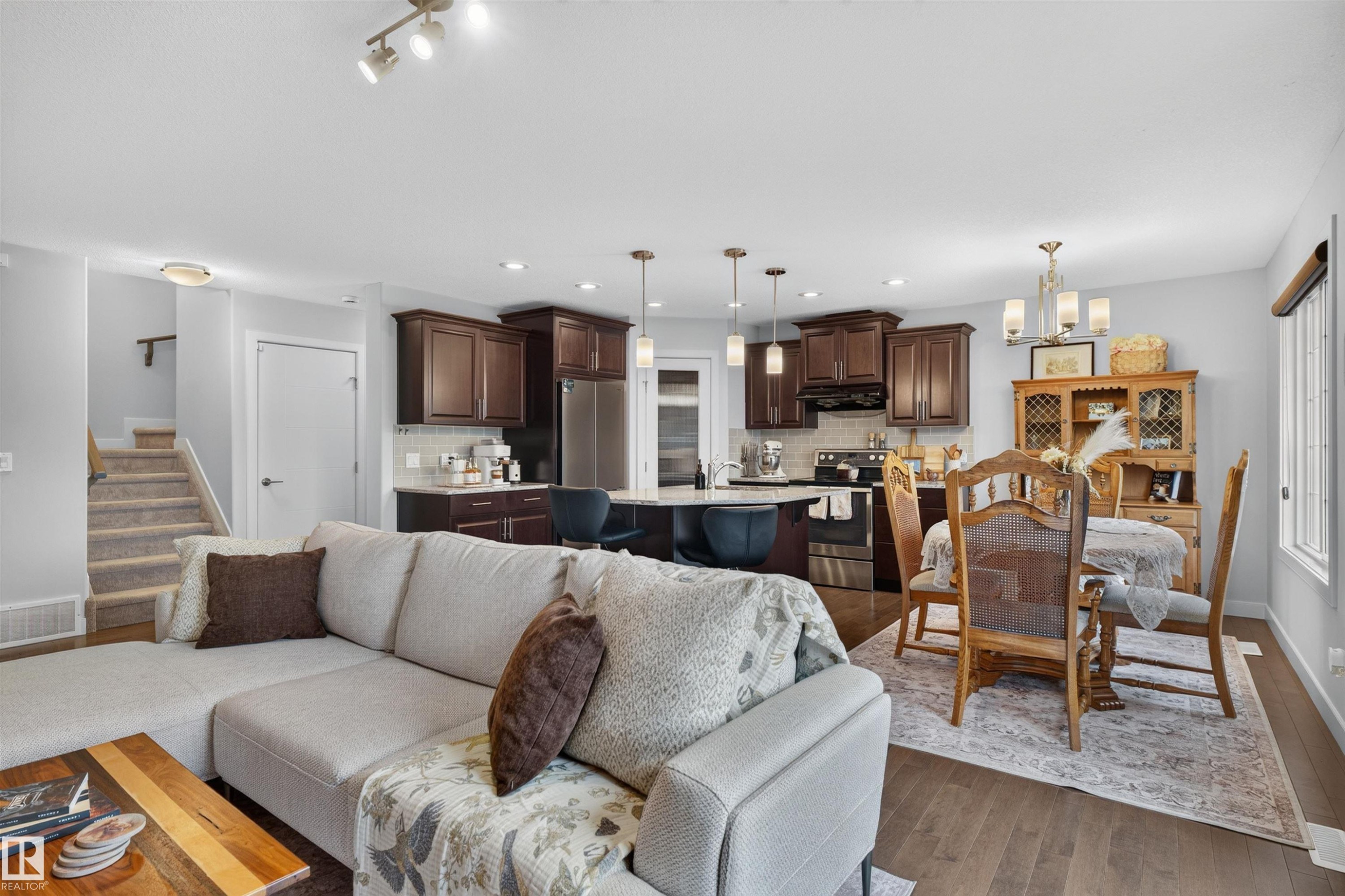 Open-concept living area featuring wood-finish flooring, a kitchen with dark wood cabinetry and stainless steel appliances, and a dining area with a chandelier - 5130 Godson Close Nw, Edmonton, AB