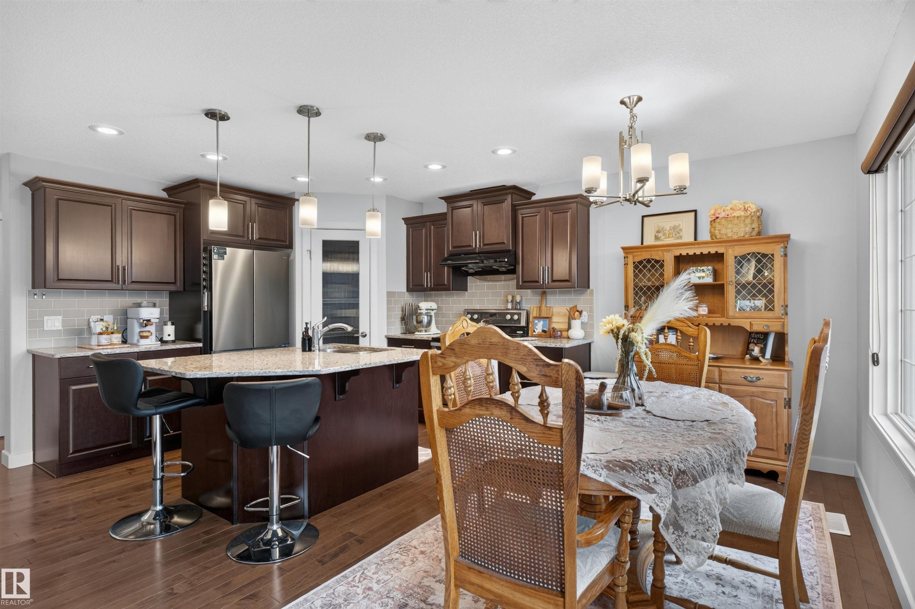 Kitchen featuring dark wood cabinetry, light-toned countertops, stainless steel appliances, and a tile backsplash - 5130 Godson Close Nw, Edmonton, AB
