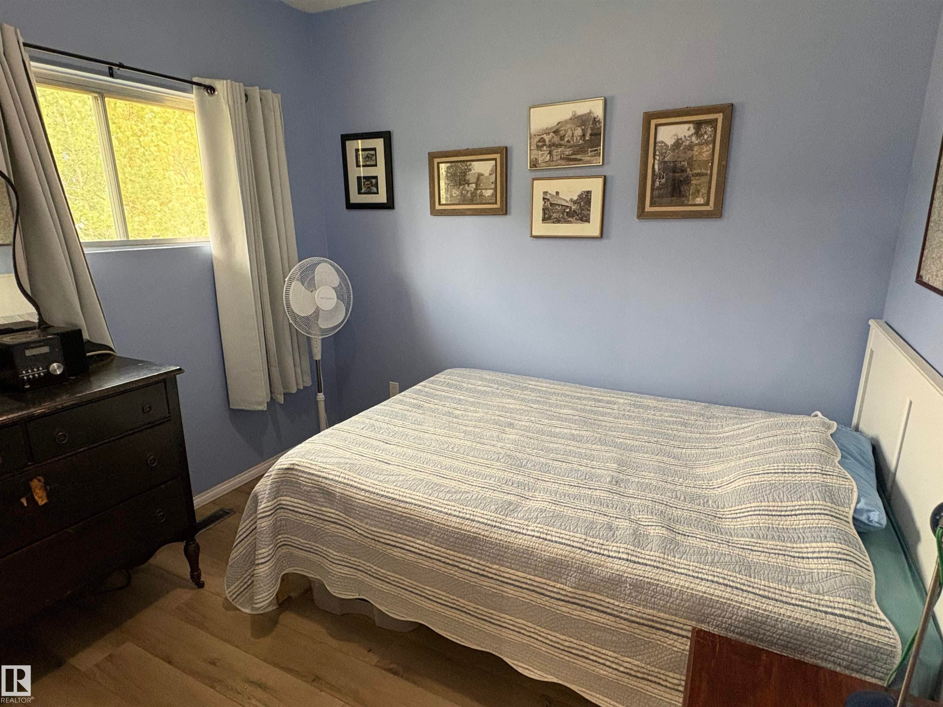 Interior room featuring a window with privacy curtains, light blue wall paint, and wood-finish flooring - 5308 50 St, Ryley, AB