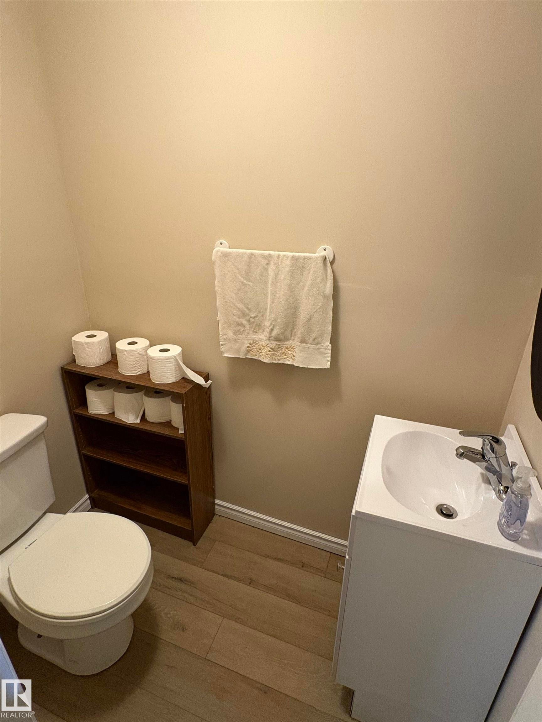 Compact powder room featuring a white pedestal sink, toilet, and wood-finish flooring - 5308 50 St, Ryley, AB