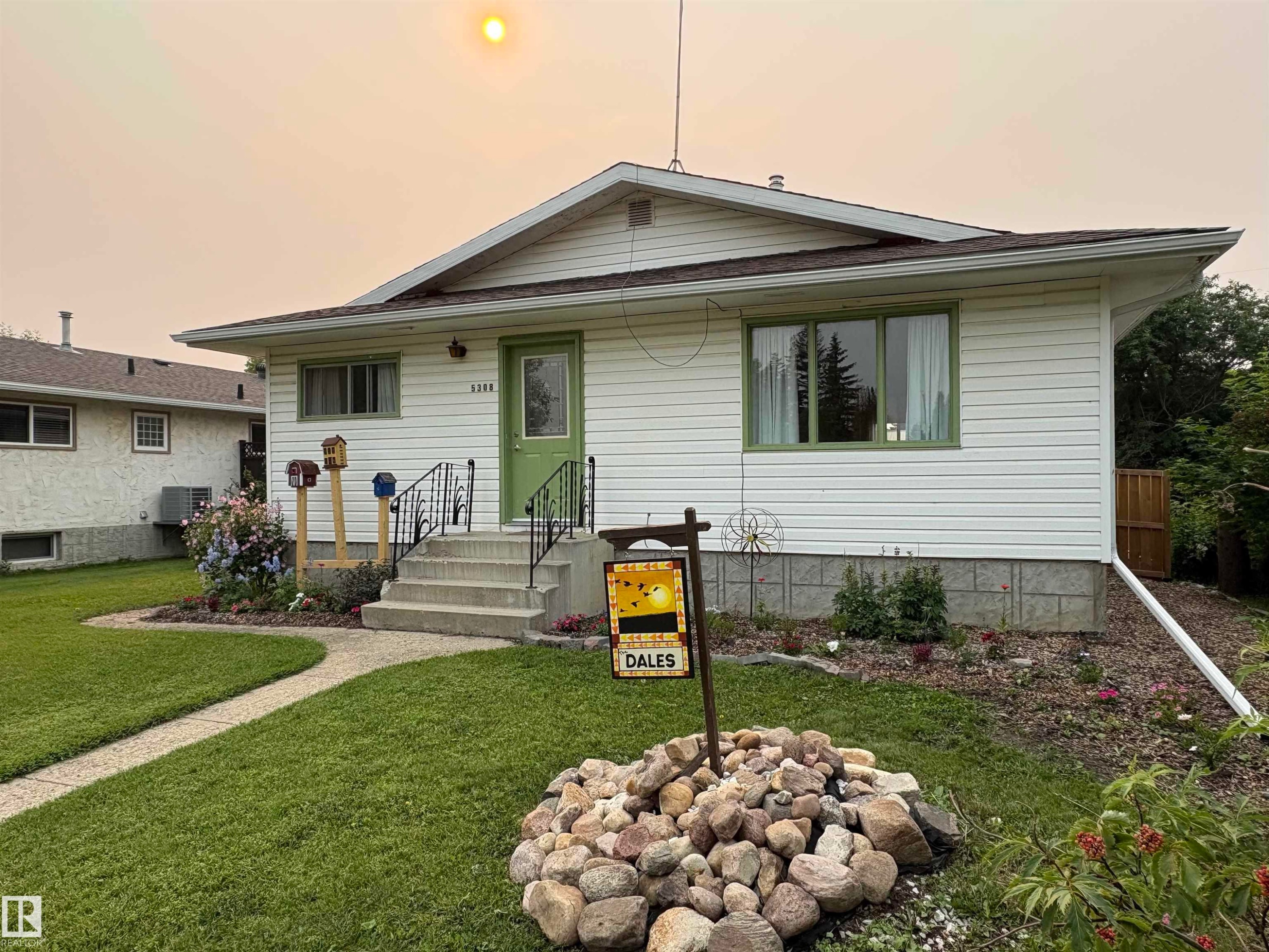 Single-story residence featuring white siding, a green entry door, and a concrete pathway - 5308 50 St, Ryley, AB