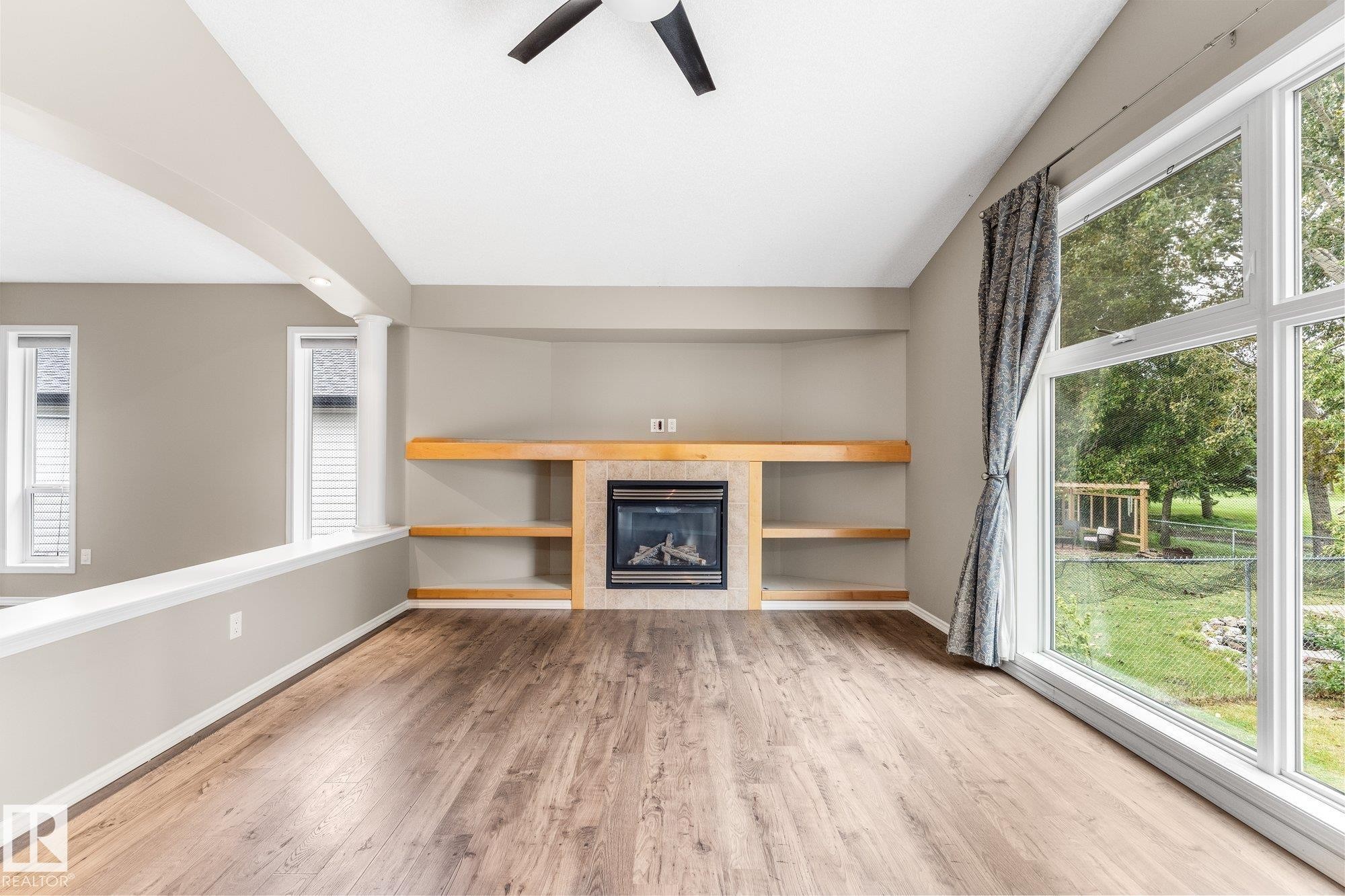 Wood-finish flooring, built-in fireplace with tile surround, integrated shelving, and large picture windows - 2060 Brennan Crescent Nw, Edmonton, AB
