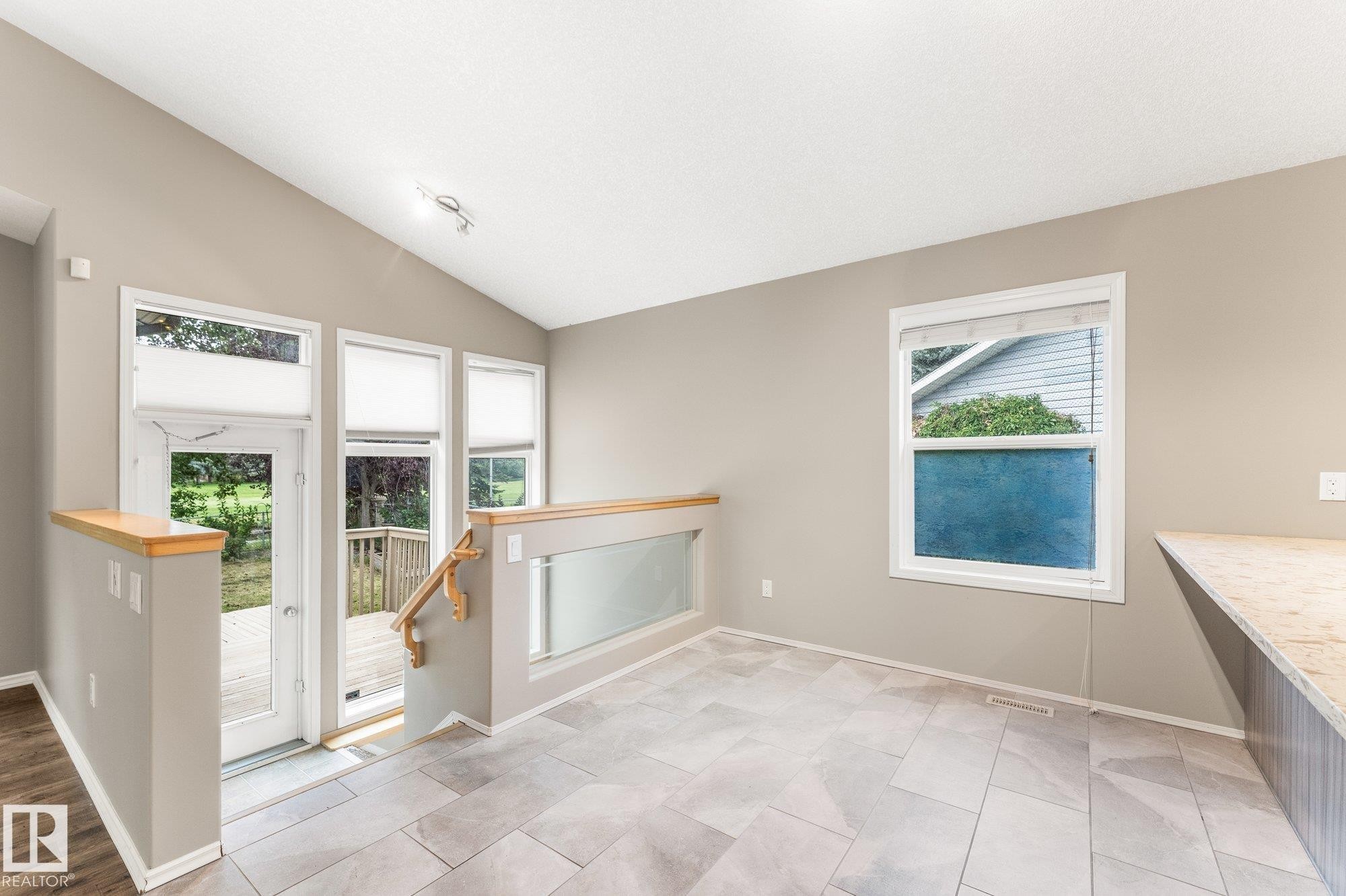 Vaulted ceiling, patio door, deck access, tile flooring, and a glass-paneled railing - 2060 Brennan Crescent Nw, Edmonton, AB