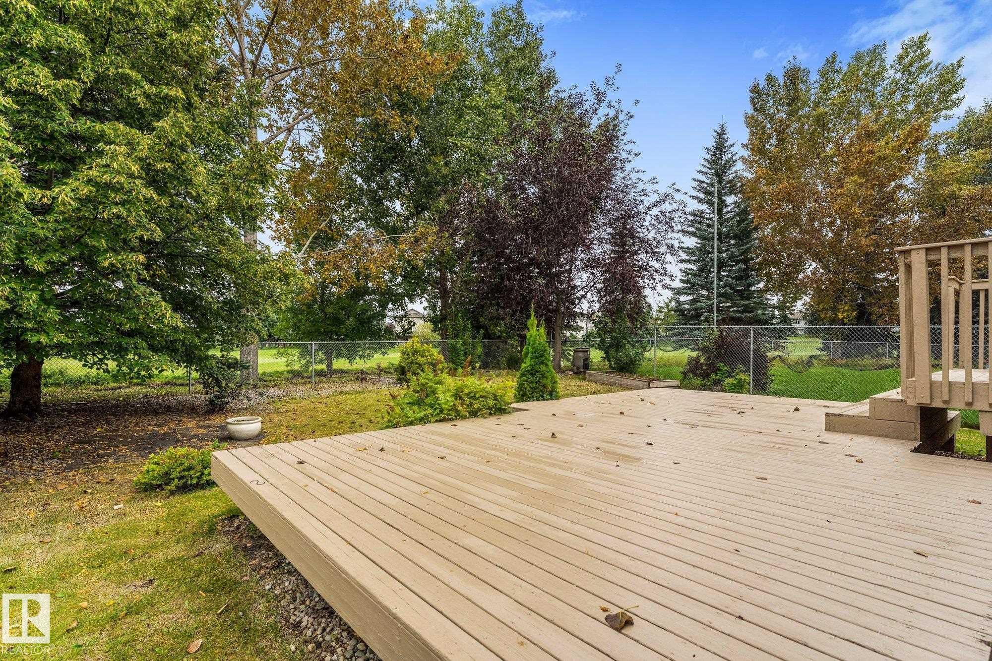 Expansive outdoor deck with integrated steps, surrounded by mature trees and a chain-link fence - 2060 Brennan Crescent Nw, Edmonton, AB