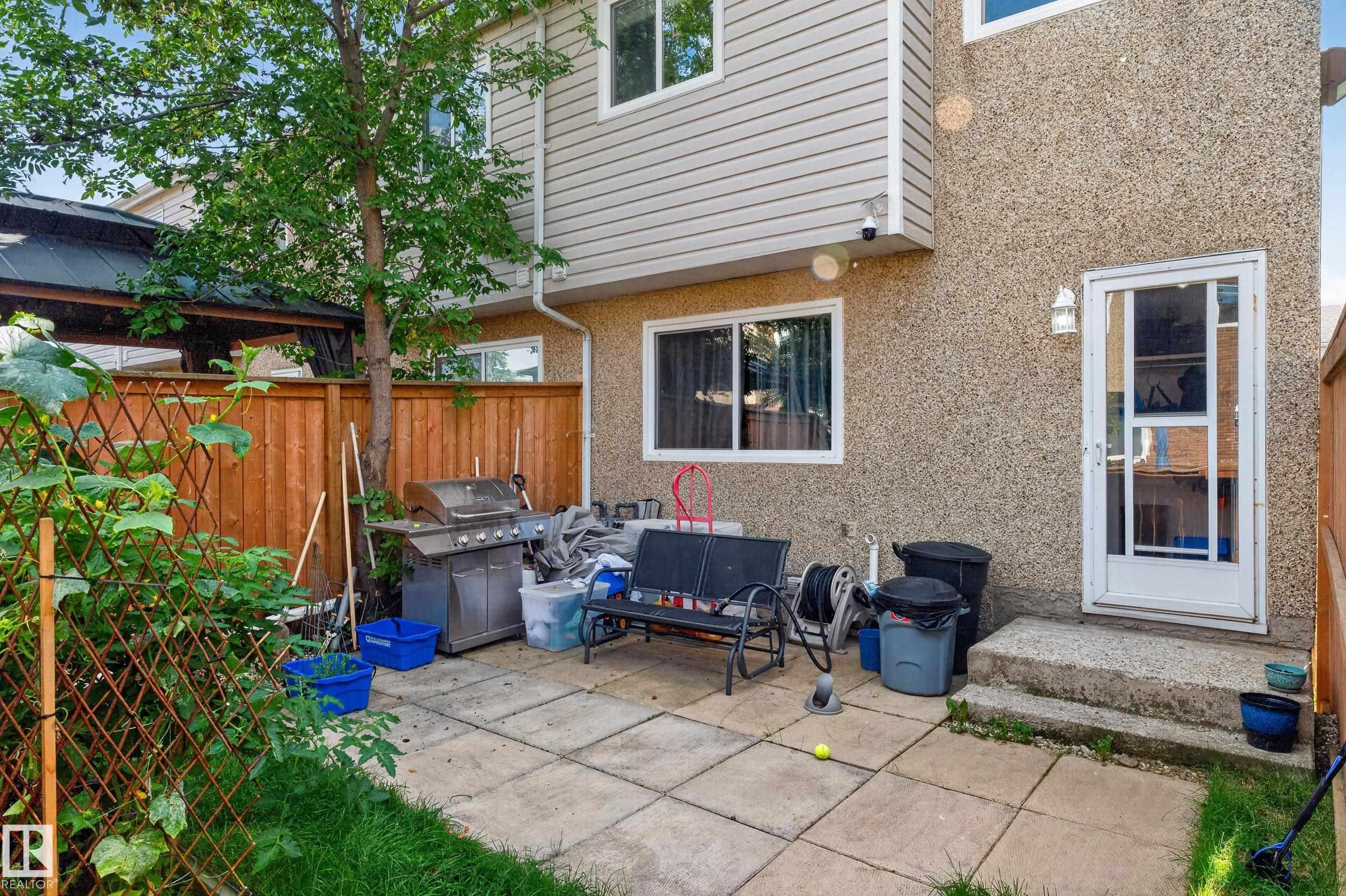 Private fenced yard with patio, mature trees, and exterior wall sconce lighting - 18319 93 Avenue Nw, Edmonton, AB