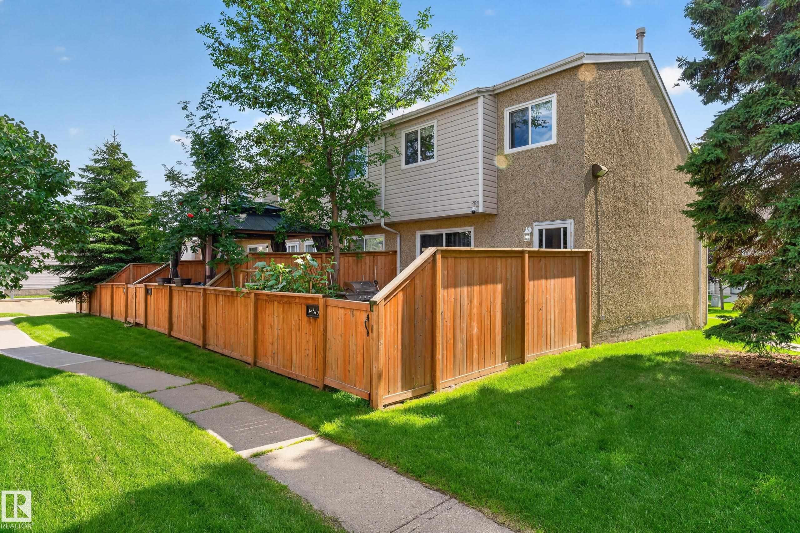 Stucco and siding exterior with multiple windows, wooden privacy fencing, and a paved walkway - 18319 93 Avenue Nw, Edmonton, AB