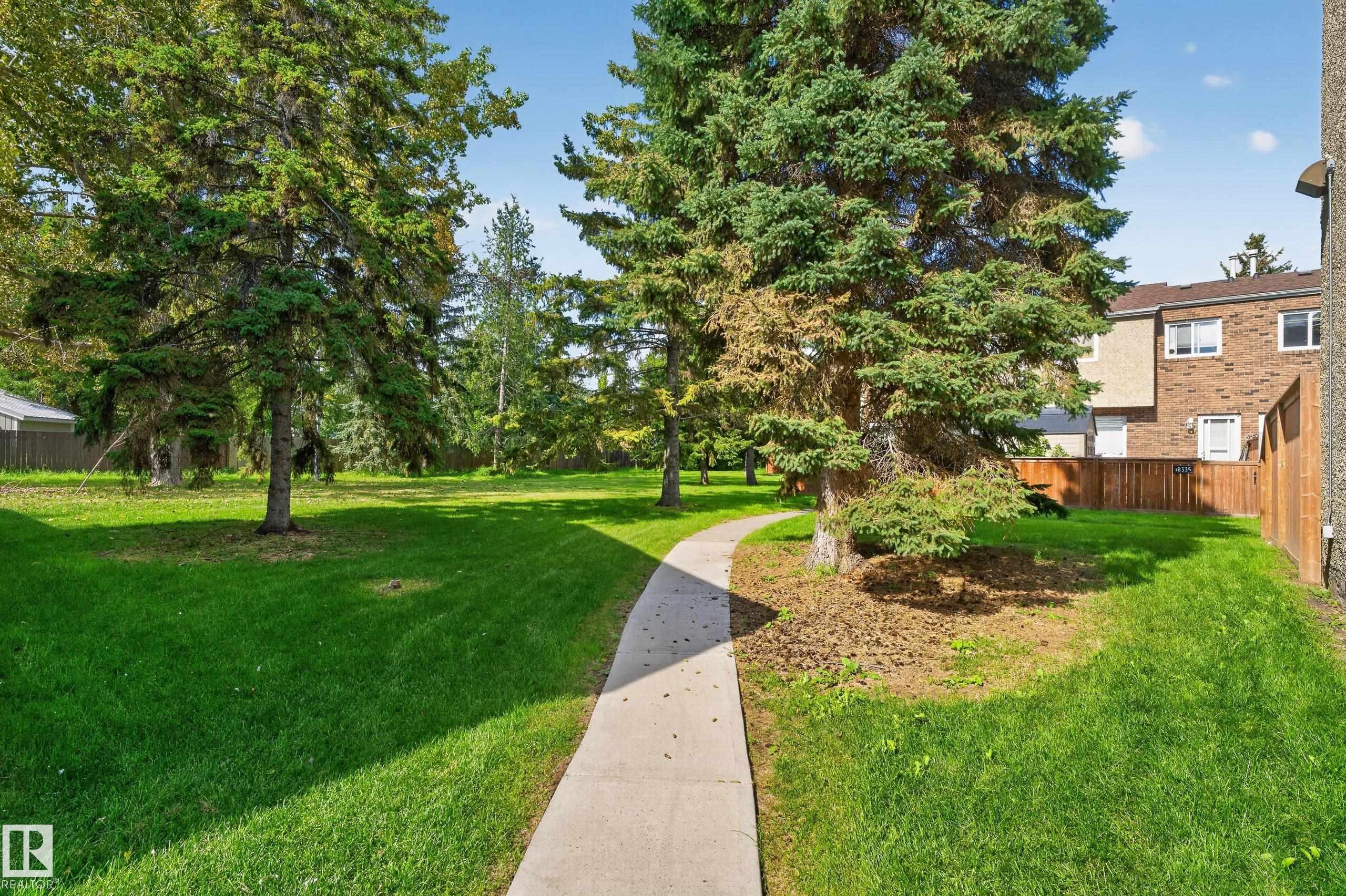 Expansive green space featuring mature evergreen trees and a paved pathway - 18319 93 Avenue Nw, Edmonton, AB
