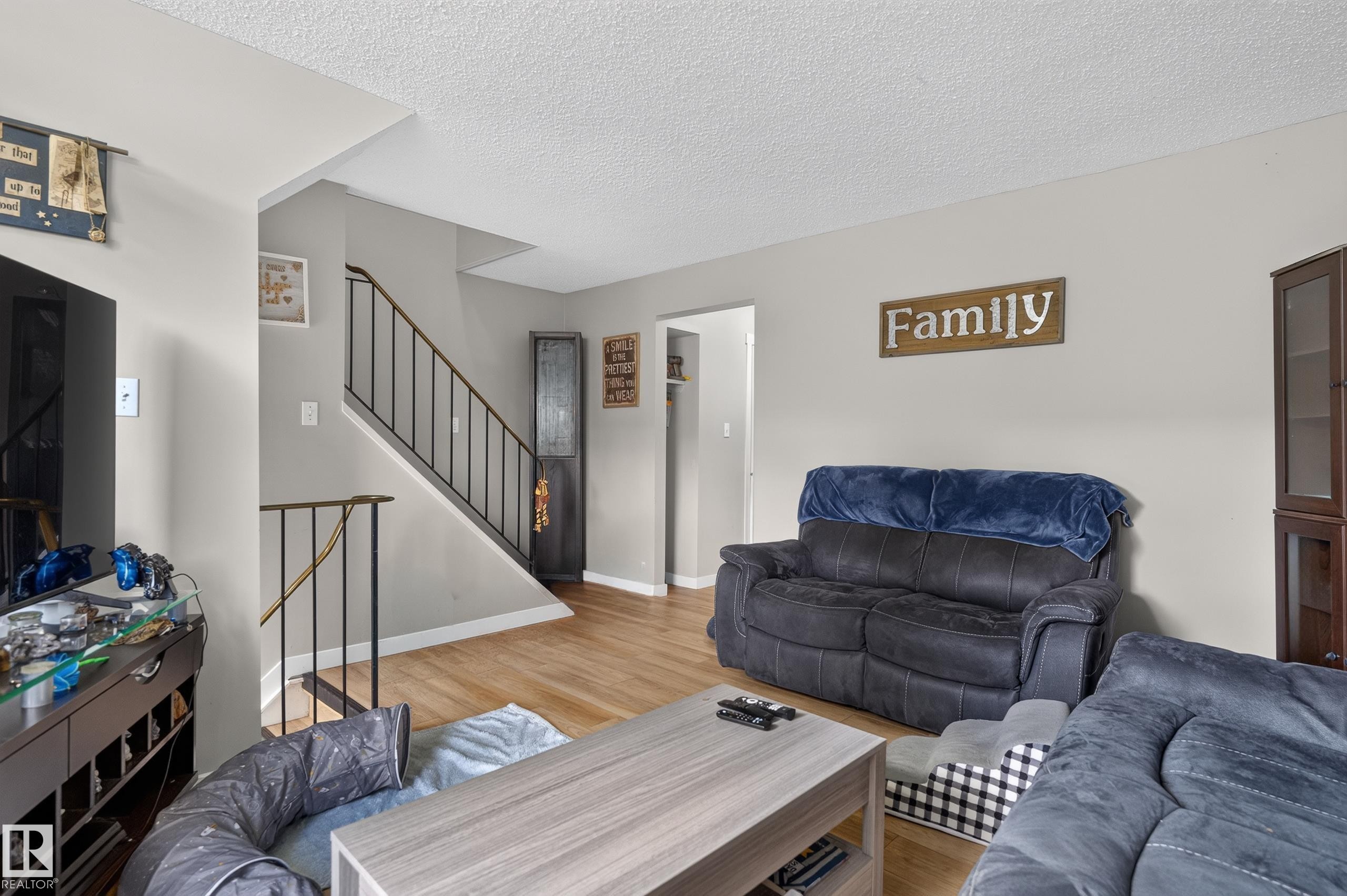 Wood-finish flooring, staircase with dark metal railings, light gray wall paint, and white trim - 18319 93 Avenue Nw, Edmonton, AB